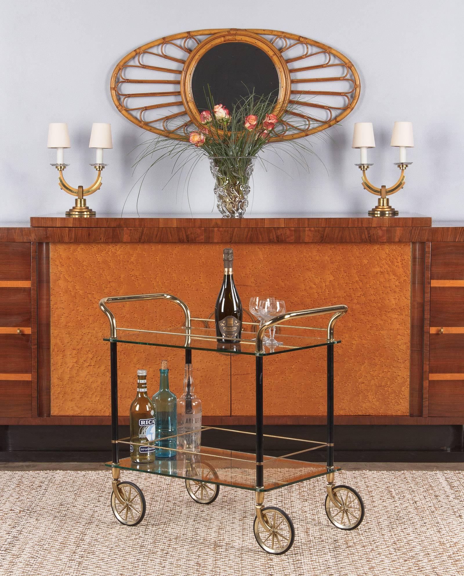 A great bar cart from Spain, circa 1980s. The vintage cart combines black metal legs with brass handles, rods and trim. Either side has a handle, instead of the typical one. Both shelves are clear glass with mirrored glass edges and trim. The bottom
