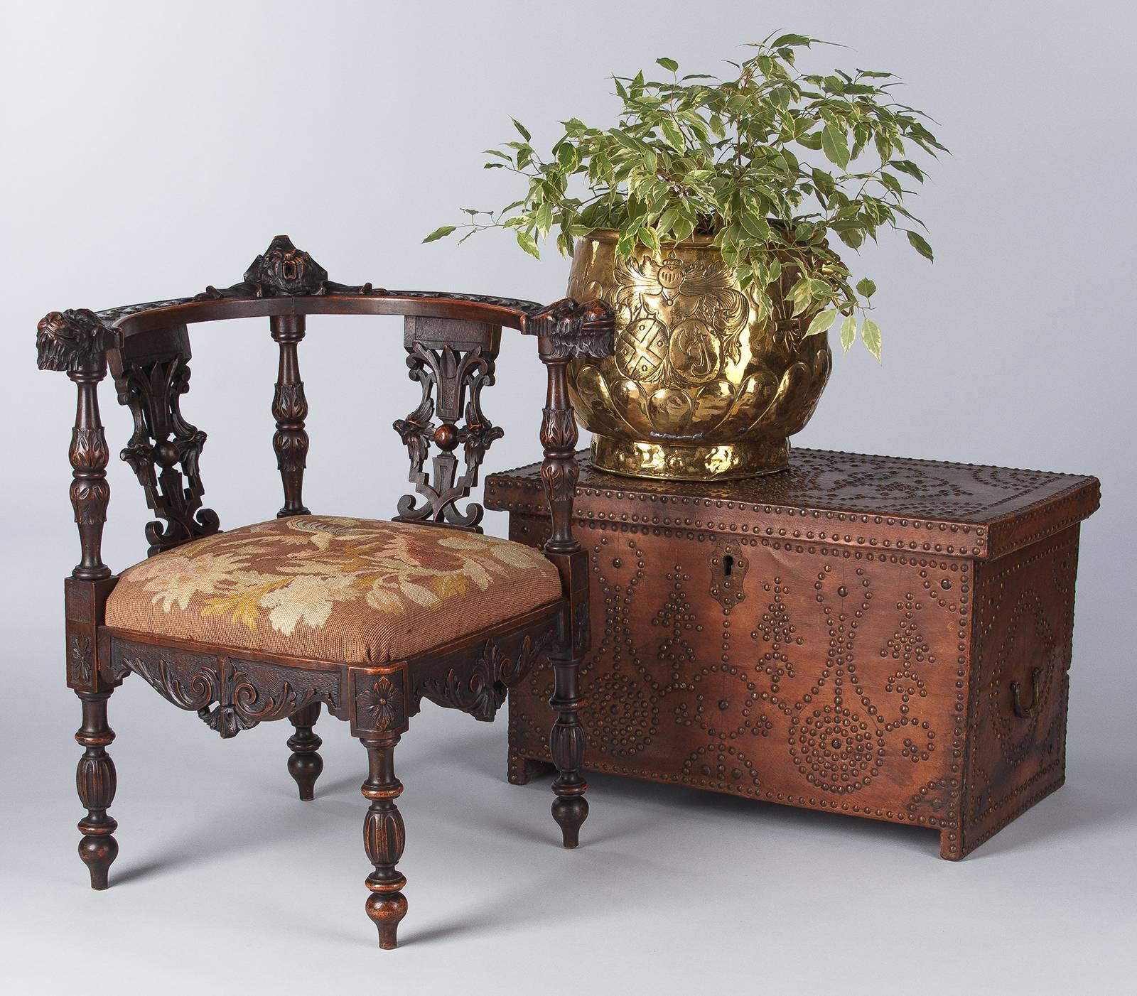 A Renaissance Revival, circa 1880s, French corner armchair made of dark walnut with abundant carvings. The rounded back features a mask at its center, fanciful dragons at the end of the armrests and phoenixes on the back. More carvings of acanthus
