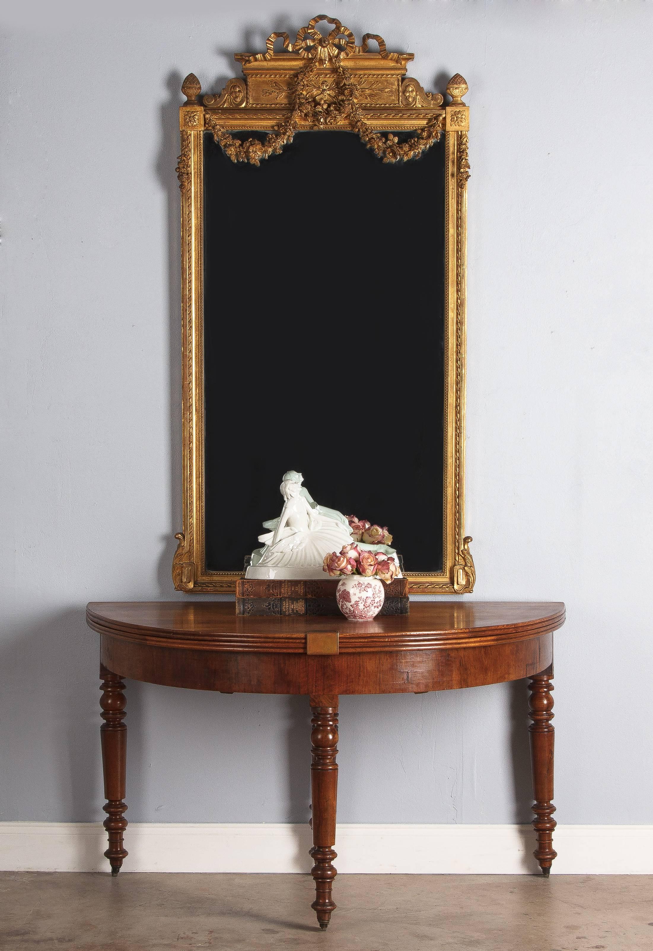 A wonderful Louis XVI style mirror, circa 1930s. The extensively carved wooden frame is fully adorned with gold leaf. Beading and notched carvings decorate the border around the beveled glass. Acanthus leaves anchor the bottom corners, while