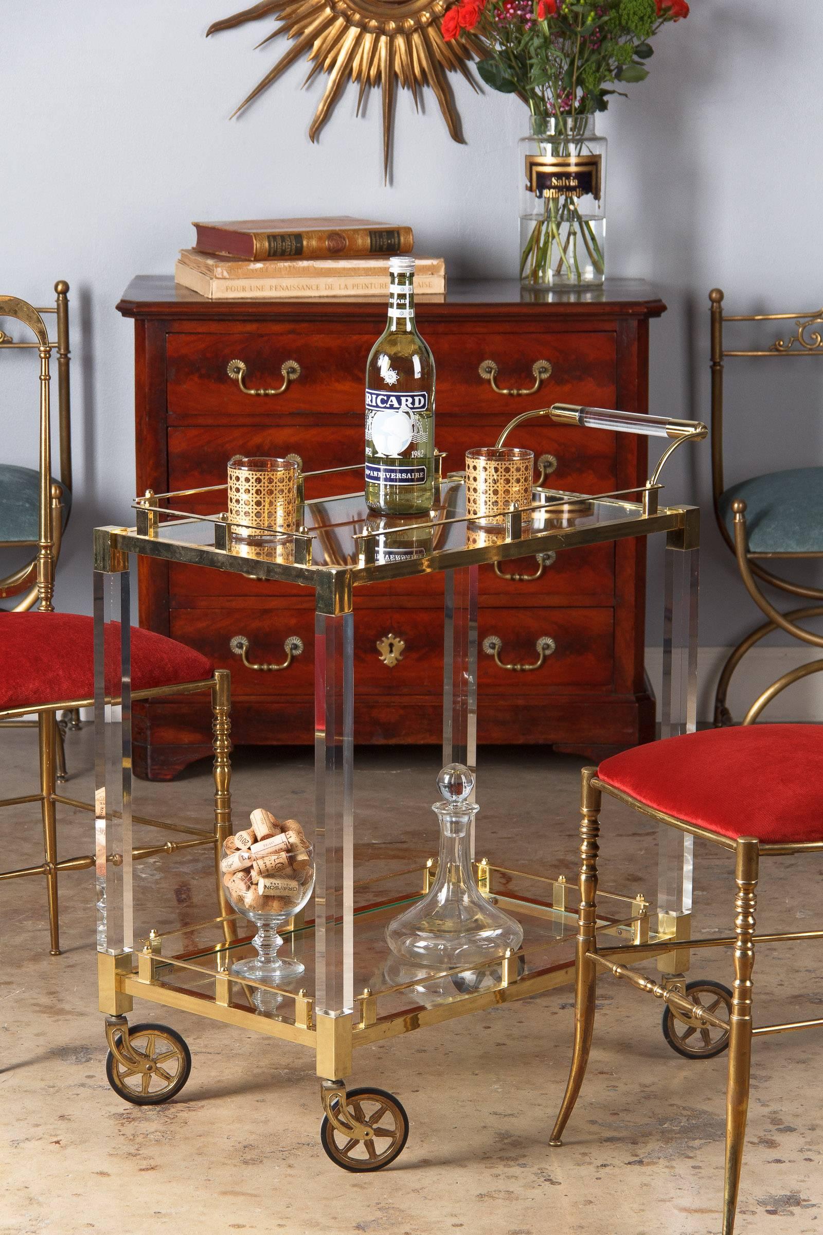 A wonderful bar cart from Spain, circa 1970s. The cart features brass rails and frames, Lucite legs and a brass and Lucite curved handle. Clear glass trays at top and bottom. It rolls on brass wheels with rubber tires.

Minor discoloration on