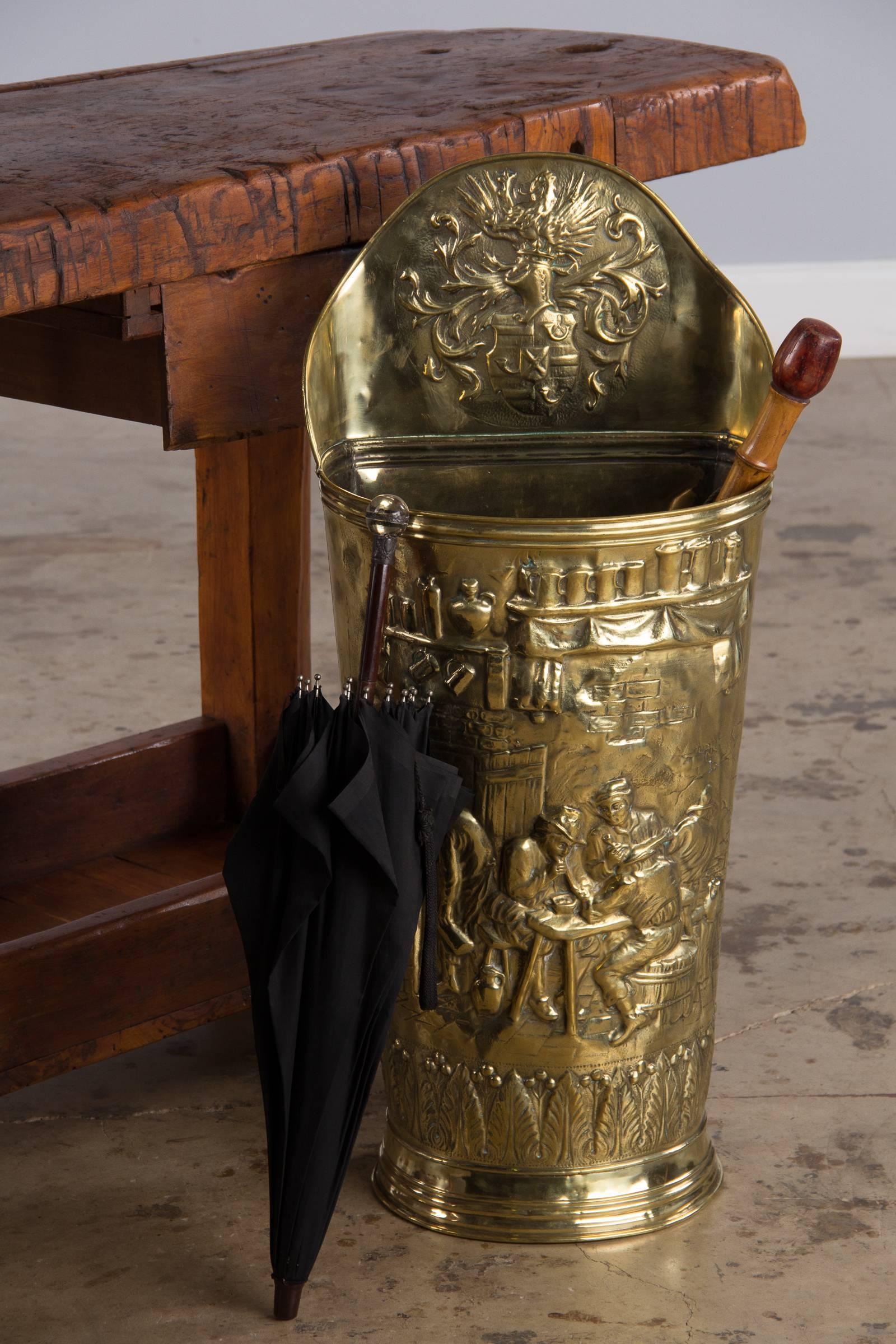 A large brass umbrella holder from Burgundy. This unique piece is shaped like a wine harvest basket from the wine regions of France. It has a raised back with a prominent repousse coat of arms containing a griffin, decorated shield and arabesques.