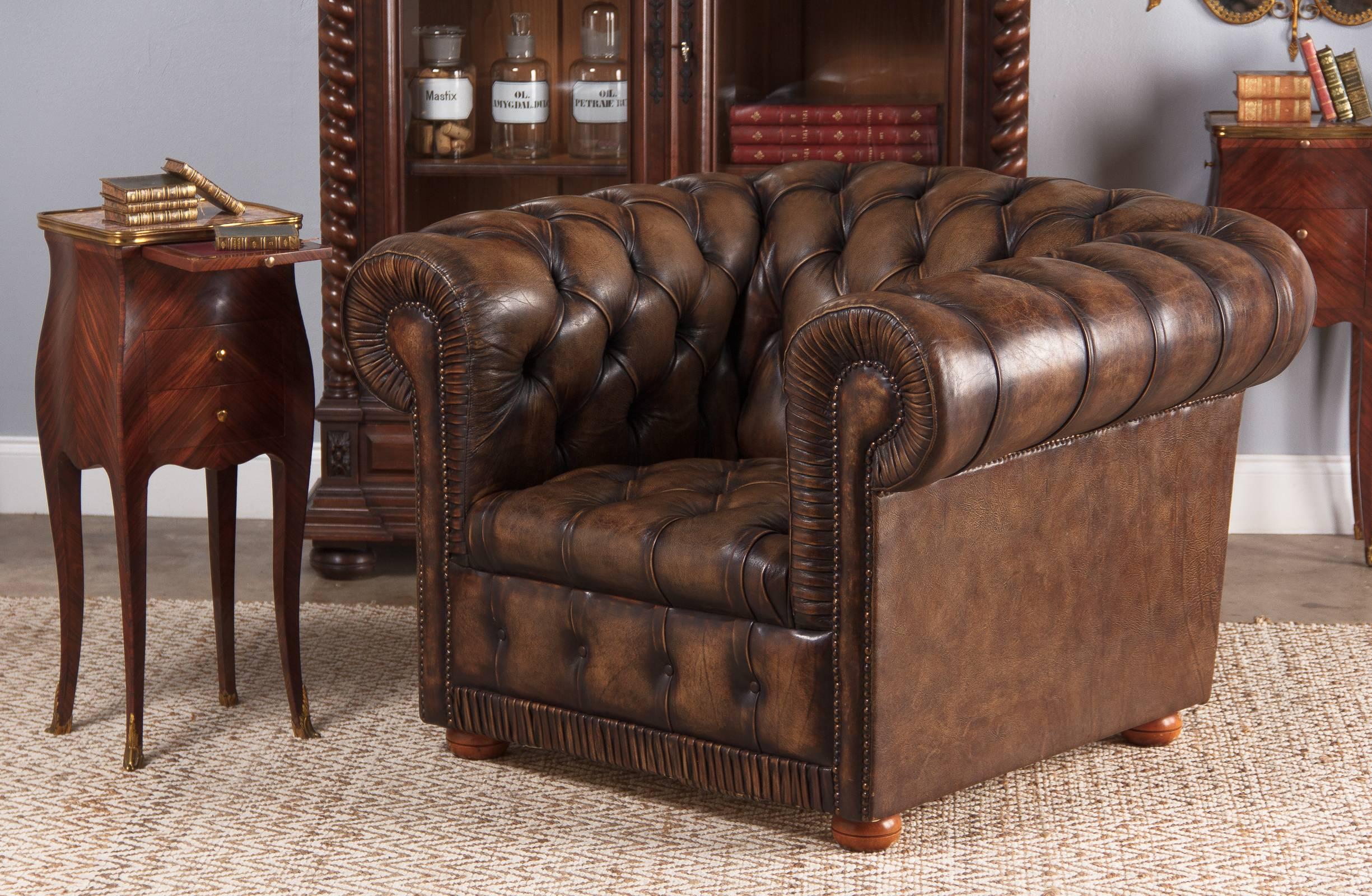 An excellent vintage Chesterfield leather armchair, circa 1960s. Beautifully conditioned brown leather, chocolate color at the tucks and buttons that fades to a light cocoa. Antique nailhead trim accentuates the chair's shape. Pleat tucks bring