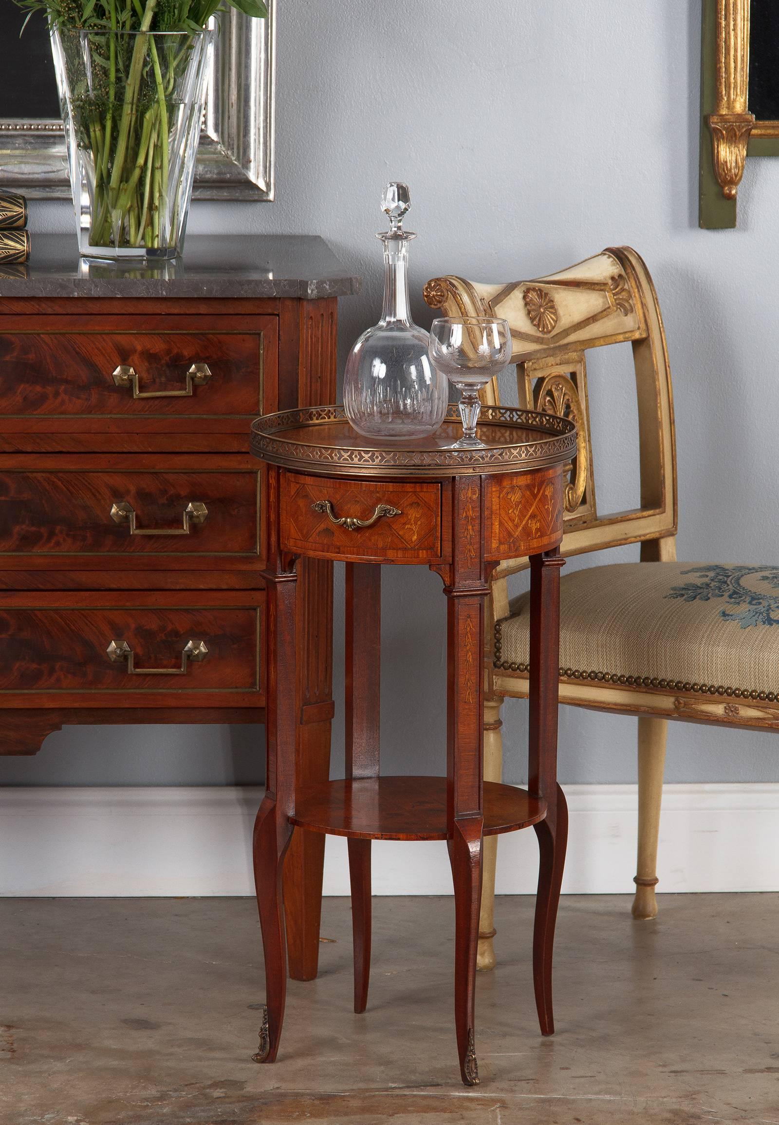 A masterfully executed marquetry side table in Louis XV/Louis XVI Transition style, from the late 1800s. The top, shelf and round sides have extensive marquetry, with a repeating floral design set into a checkerboard of alternately orientated wood