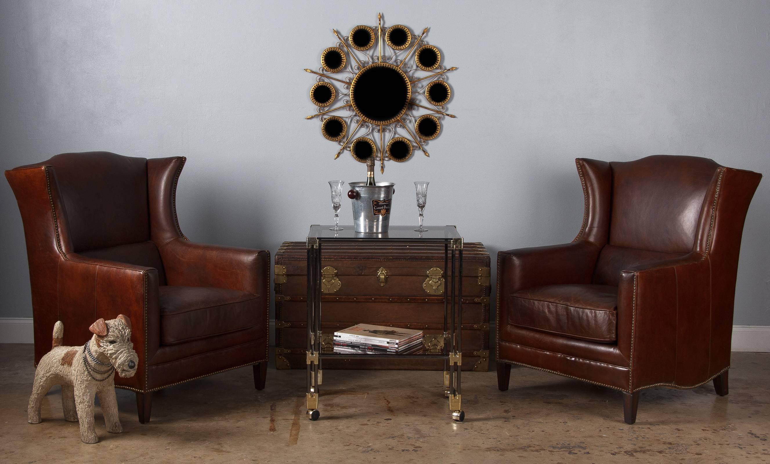 A pair of French wingback armchairs in rich brown leather, circa 1980. These armchairs have wonderful silhouettes, with a slight flare to the wingbacks, scalloped tops and curved edges along the lower sides. The leather is a deep, chocolate brown