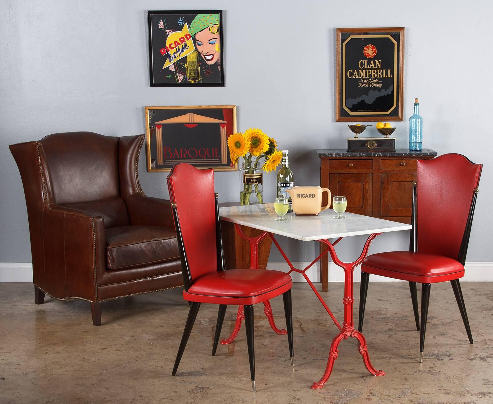 A Mid-Century French iron bistro table with marble top, circa 1950s. The Classic iron frame, with its scroll details and X-shaped stretcher, is painted a snappy, brilliant red. White marble slab with grey veins criss-crossing throughout, .75"