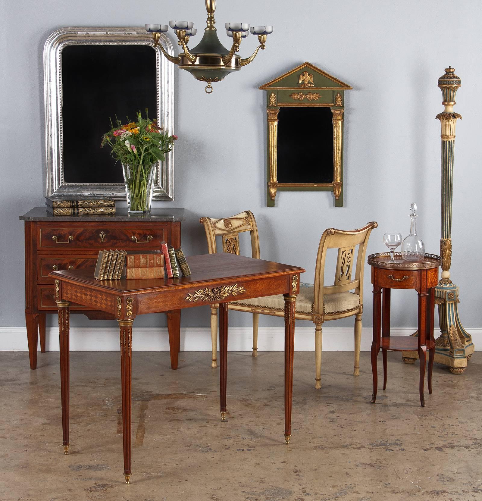 An ornate Louis XVI style desk or side table with extensive marquetry and gilt bronze ornamentation, from the late 1800s or early 1900s. Created as a writing desk for the bedroom, this piece is small in scale, but packs in loads of details. The top