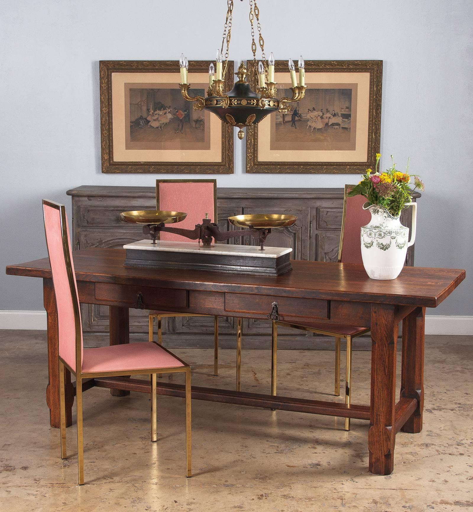 A substantial oak French country farm table or desk, circa 1900s. Dark stained oak with rustic peg construction. The top is made from seven thick boards joined by splines. Four stout post legs have their corners notched and carved into long, angled
