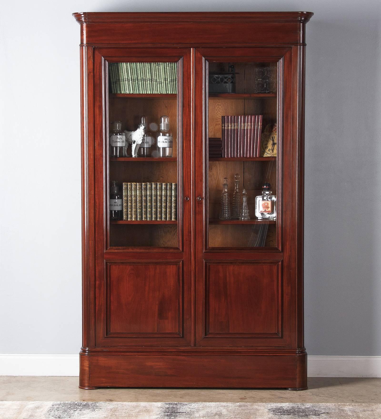 A large, debonair mahogany bookcase from the Restoration period, circa 1820. The Cuban mahogany is a glossy, rich and warm-toned brown. Two front doors with original glass and panelled lower portion have molded trim throughout. Handsome round wooden
