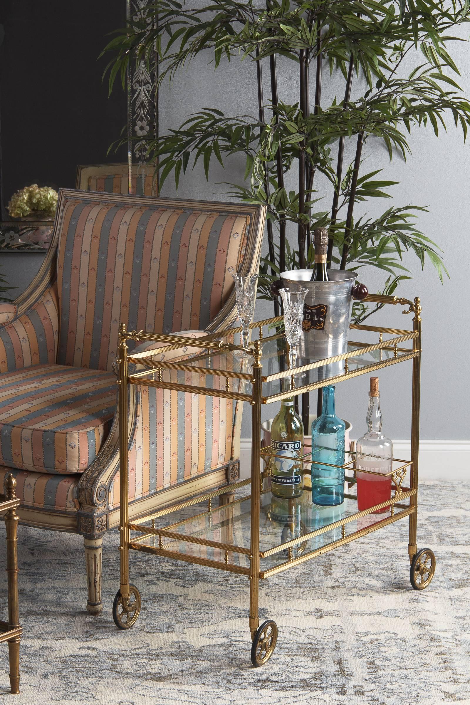 A fabulous midcentury brass and glass two-tiered bar cart attributed to Maison Baguès, circa 1950. Fluted brass frame, legs and handles. Each end has its own decorated handle, fluted at the center with textured and gracefully curled scrolls that