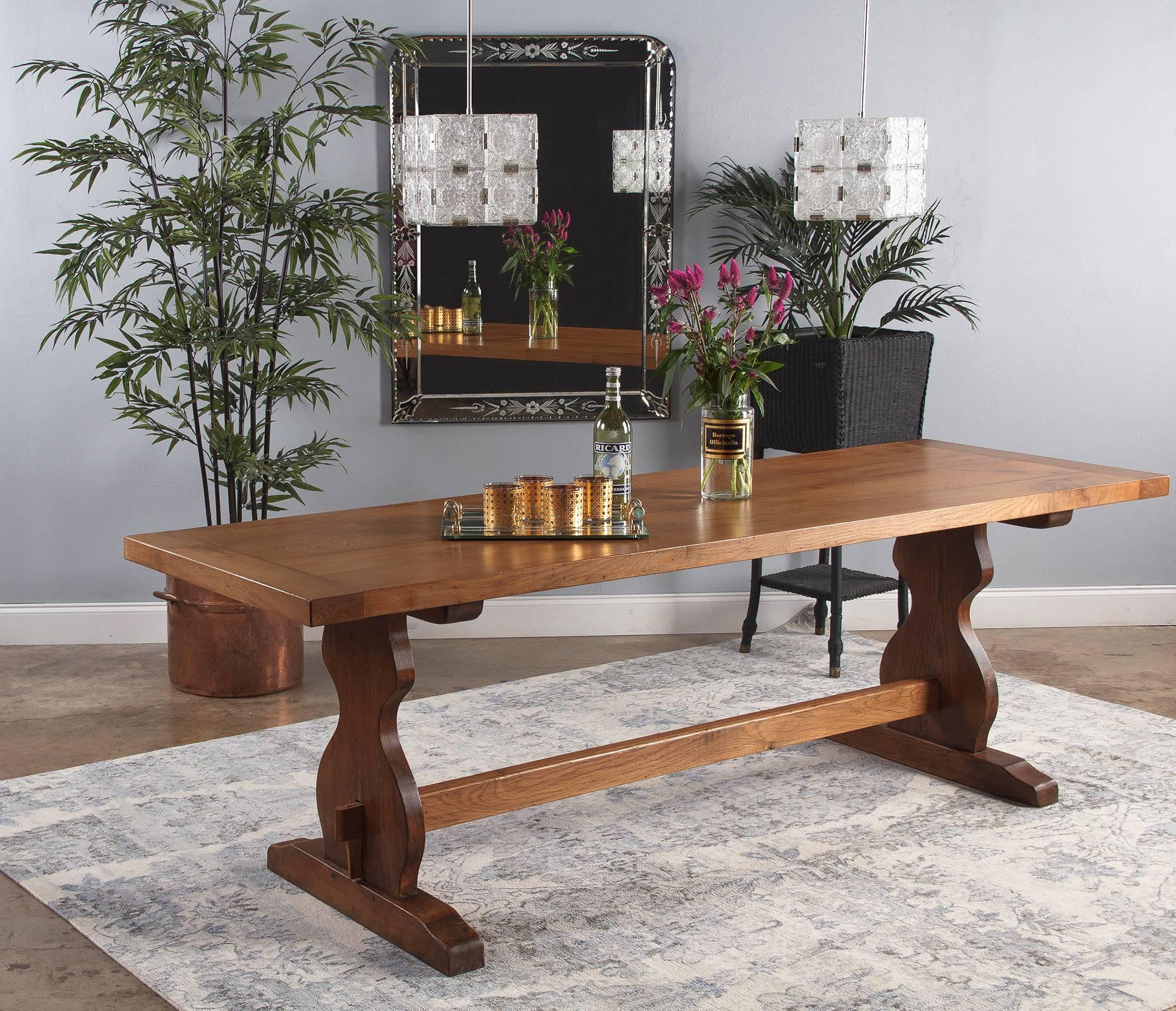 An charming French golden oak trestle dining table, circa 1940. Simple, attractive construction with two broad boards joined for the top, capped by two end pieces. The tenon and key stretcher connects to the two solid legs, who's shape recalls a