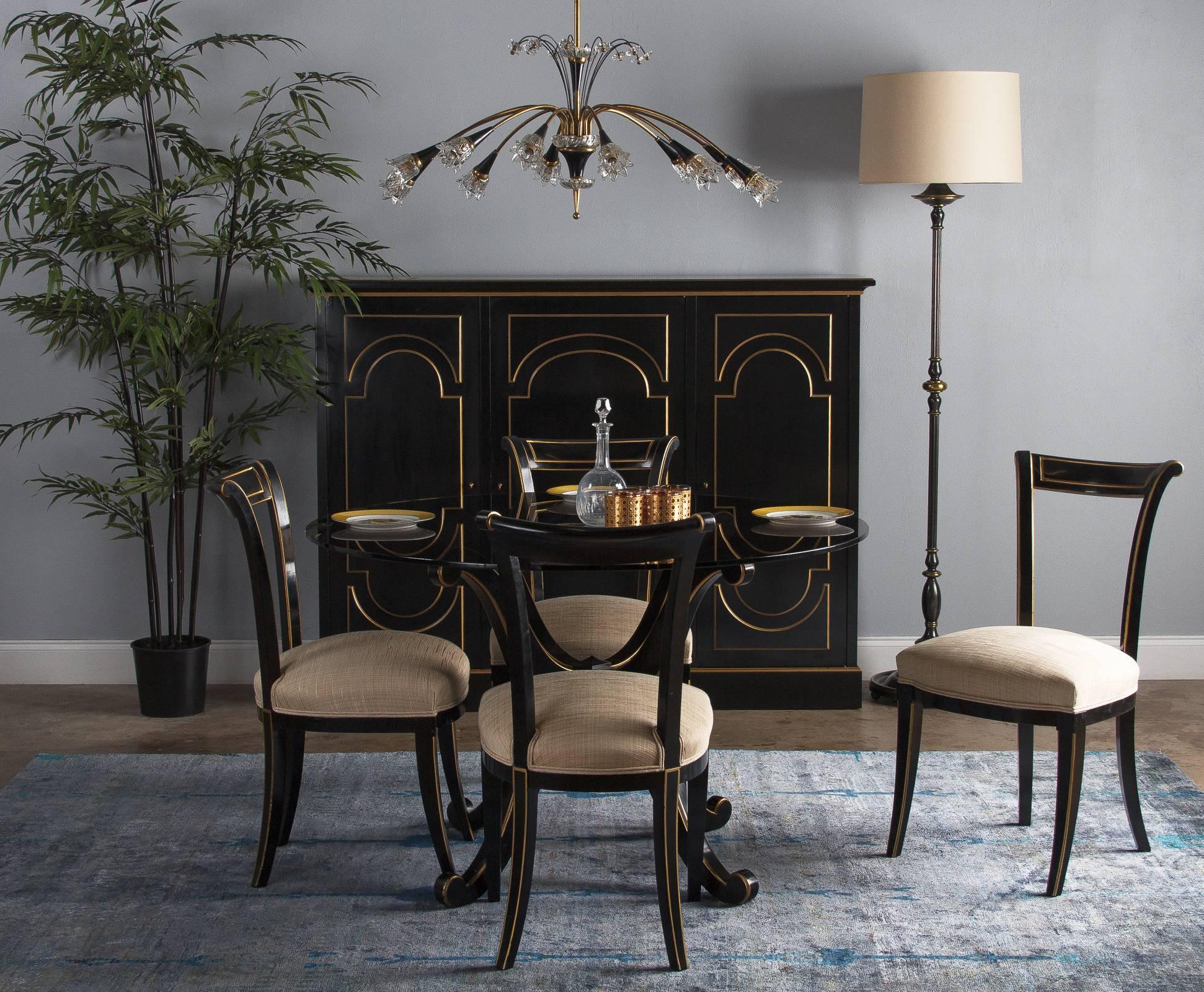 A set of four urbane neoclassical style varnished ebony chairs from designer Maurice Hirsch, circa 1950s. Glossy black varnish coats the wood frame. The back flares out and back gently, ending in scrolled corners and connected by a single slat at