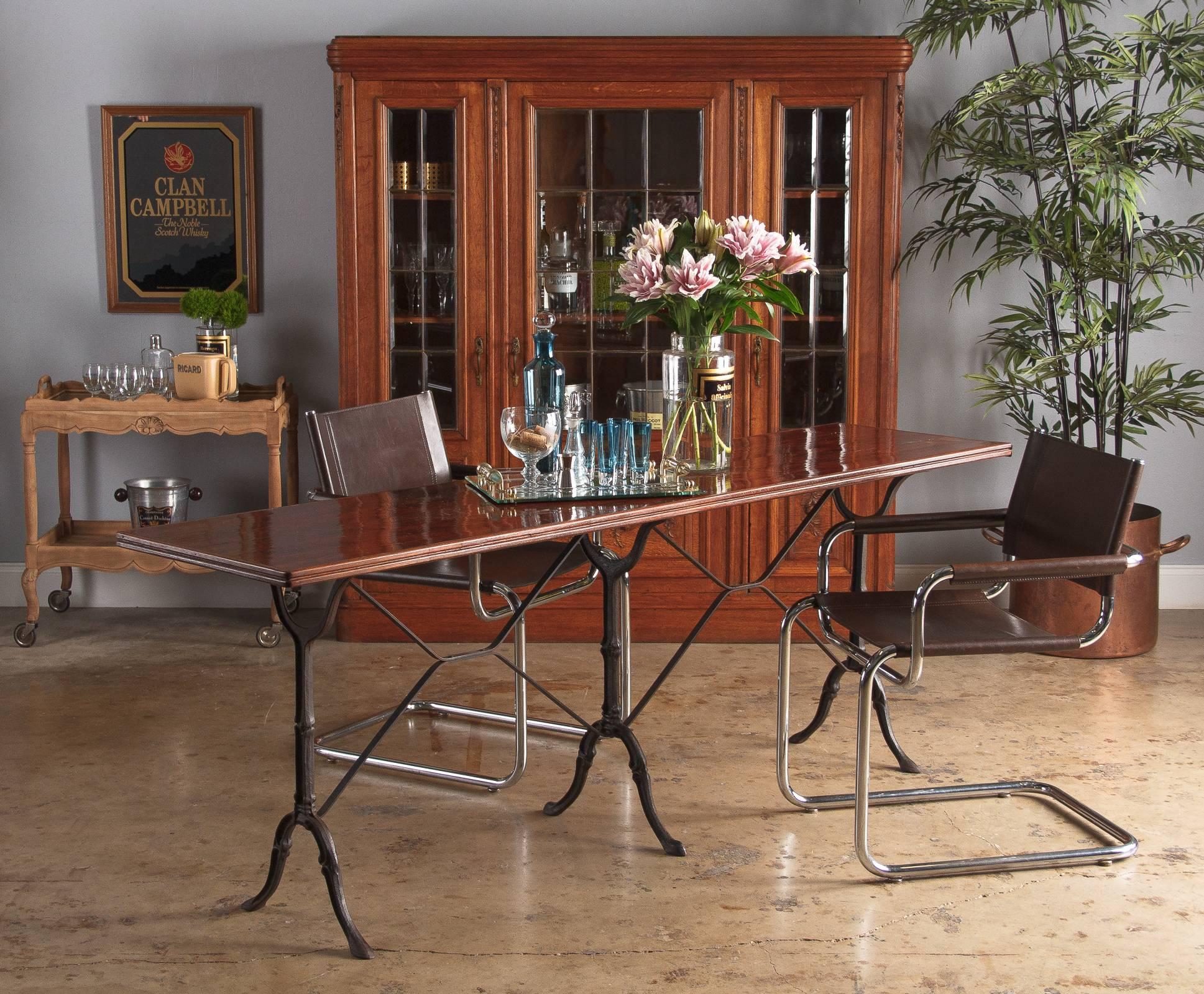 A long French bistro table with lacquered wood top and wrought iron legs, vintage, circa 1920s. The narrow pine top has a red-toned lacquer and high gloss finish. Molded wood edges are affixed to the sides along the table. Three sets of dainty black