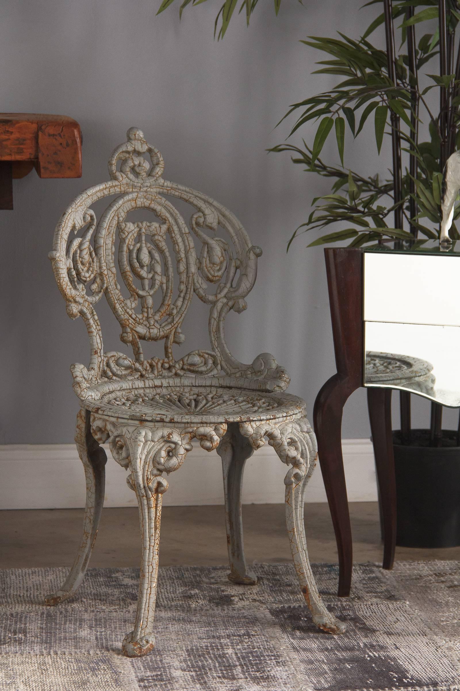 A pair of ornate cast iron painted garden chairs, French, circa 1950. Victorian in style, having hot air balloon backs with pierced scroll decoration. The circular seats feature pierced sunburst motif. Curved legs attach to the seats with broad