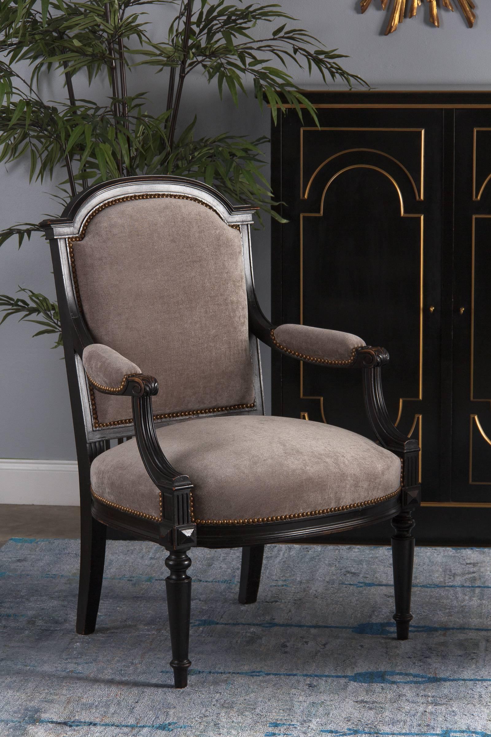 A Napoleon III period armchair in ebonized pear wood. It has been recently re-upholstered in a fine neutral taupe with a velvety feel, finished with antiques nails. The wide, comfortable armchair has an arched top, curved and fluted armrests with