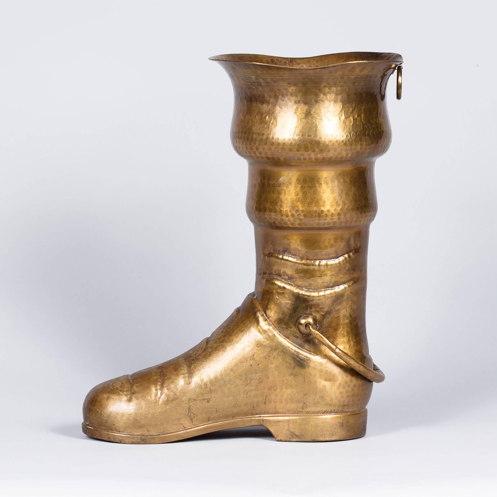 A whimsical umbrella holder in the form of a brass boot, French, circa 1900. Brilliant hammered brass is shaped into a low-heeled boot with a tiered, widening leg. The rim flares out and there is a handle attached at the ankle, as well as a small