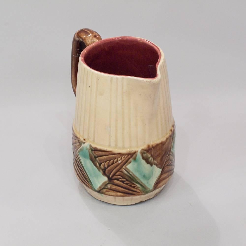 An Art Deco era barbotine, or majolica, ceramic pitcher with colorful glazing from Orchies in Northern France. The conical body is slightly tapered near the mouth and has a straight, angled spout. It is etched with vertical ribs in groups of six and