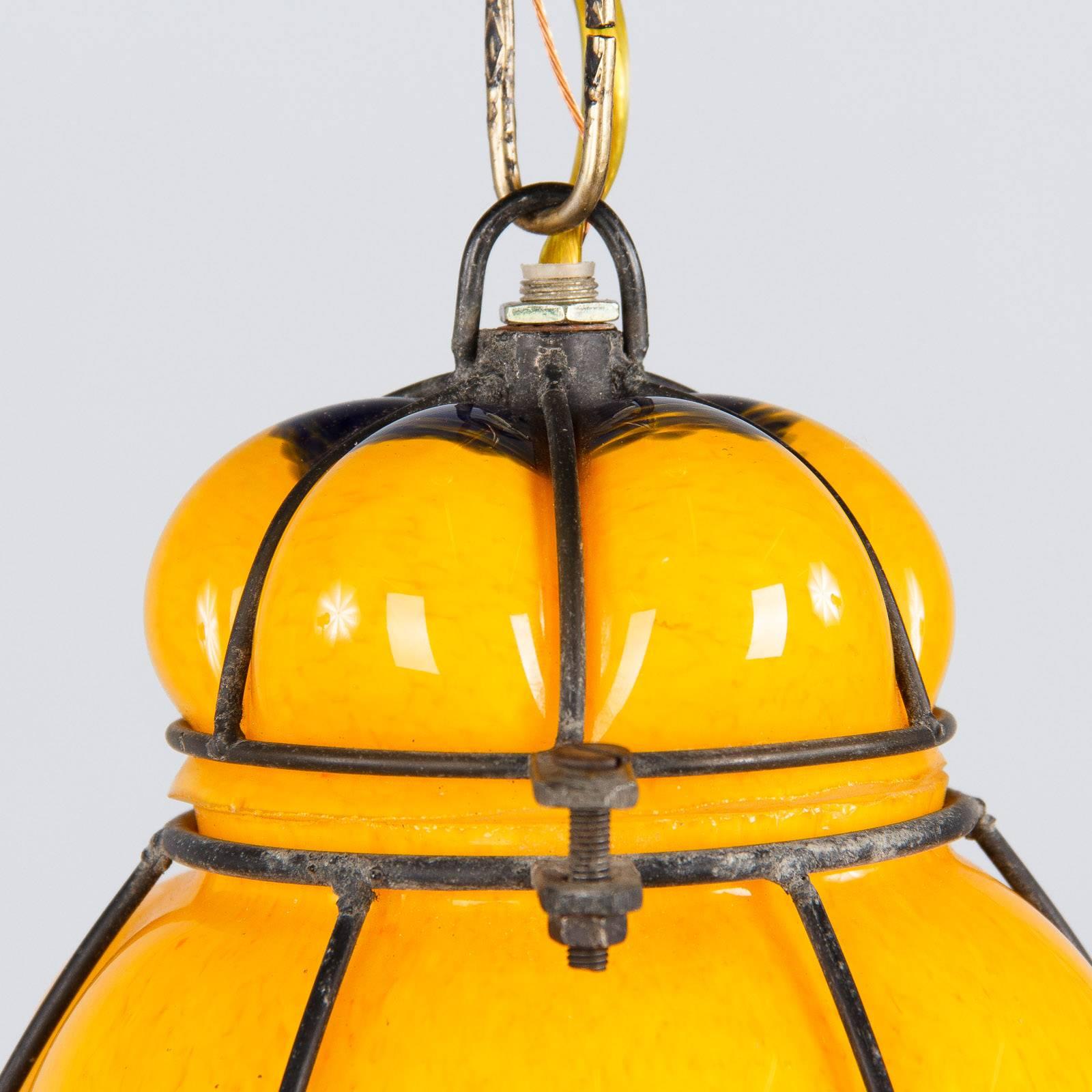A colorful Mid-Century caged Murano glass pendant hanging lantern. Opaque yellow and dark green handblown glass with red/orange flecks, caged in a black metal. Top unhinges to place or change single medium size bulb (up to 100 watts). Chain and