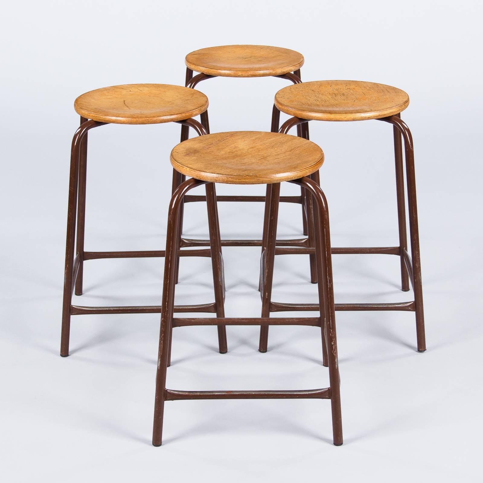 A set of four Mid-Century Industrial stools that were used in schools. The stools are stackable. They are made of tubular metal painted brown with pine seats. The seats are 12.5