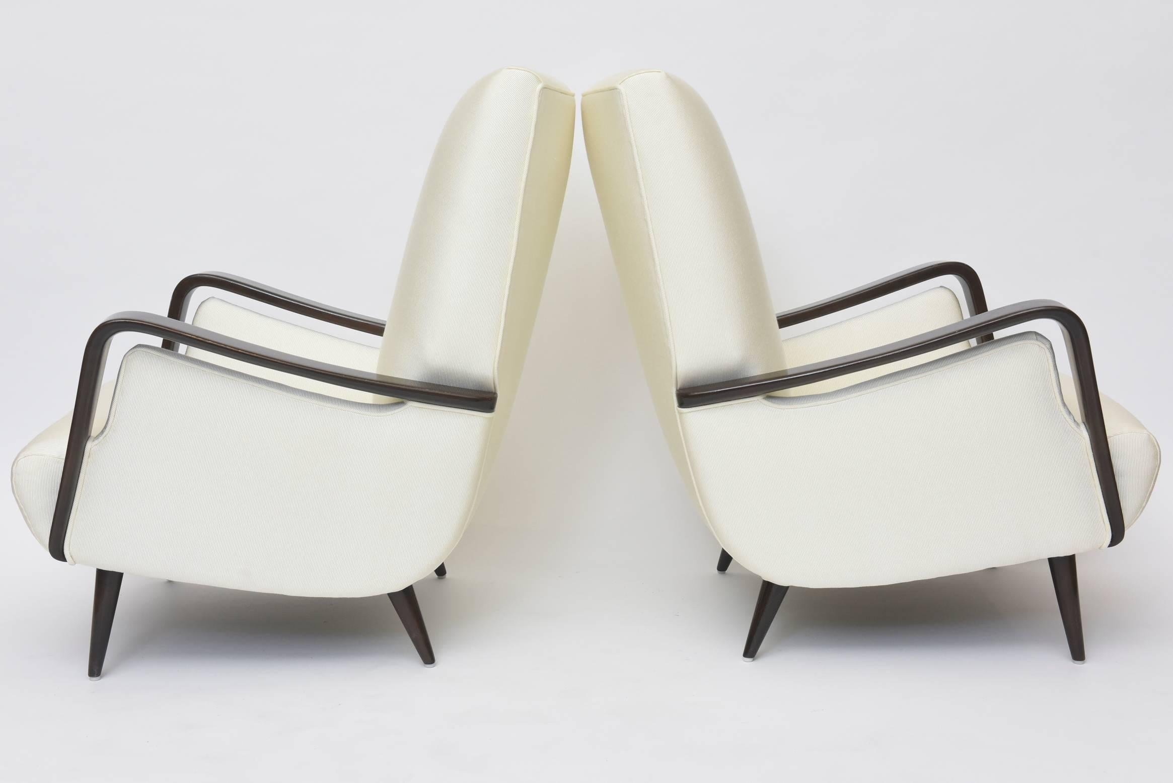 This pair of club chairs was designed by Melchiorre Bega in Italy during the 1950s. The pieces are made from dark walnut and features round tapered legs, splayed back feet and luxurious alabaster ivory colored upholstery.