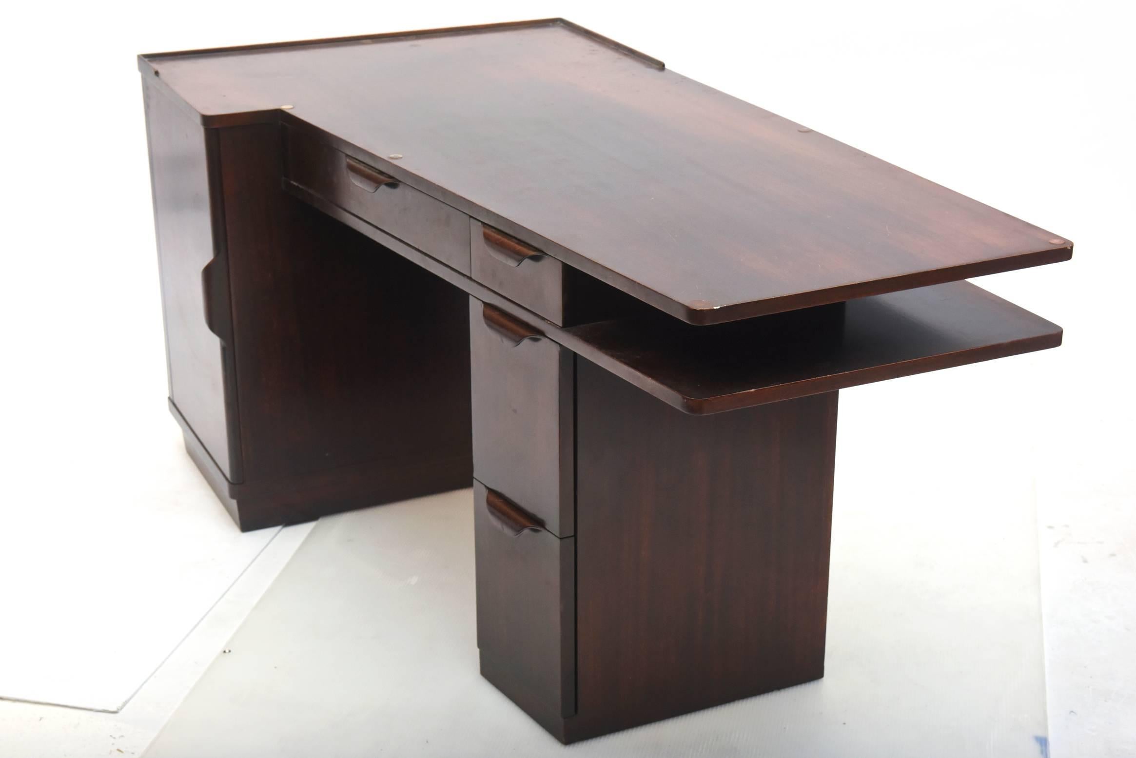 The shaped cantilevered top above a cabinet door with shelves, flanked by a series of three graduating drawers, centred by a pencil drawer, with a parallel shelf, the 