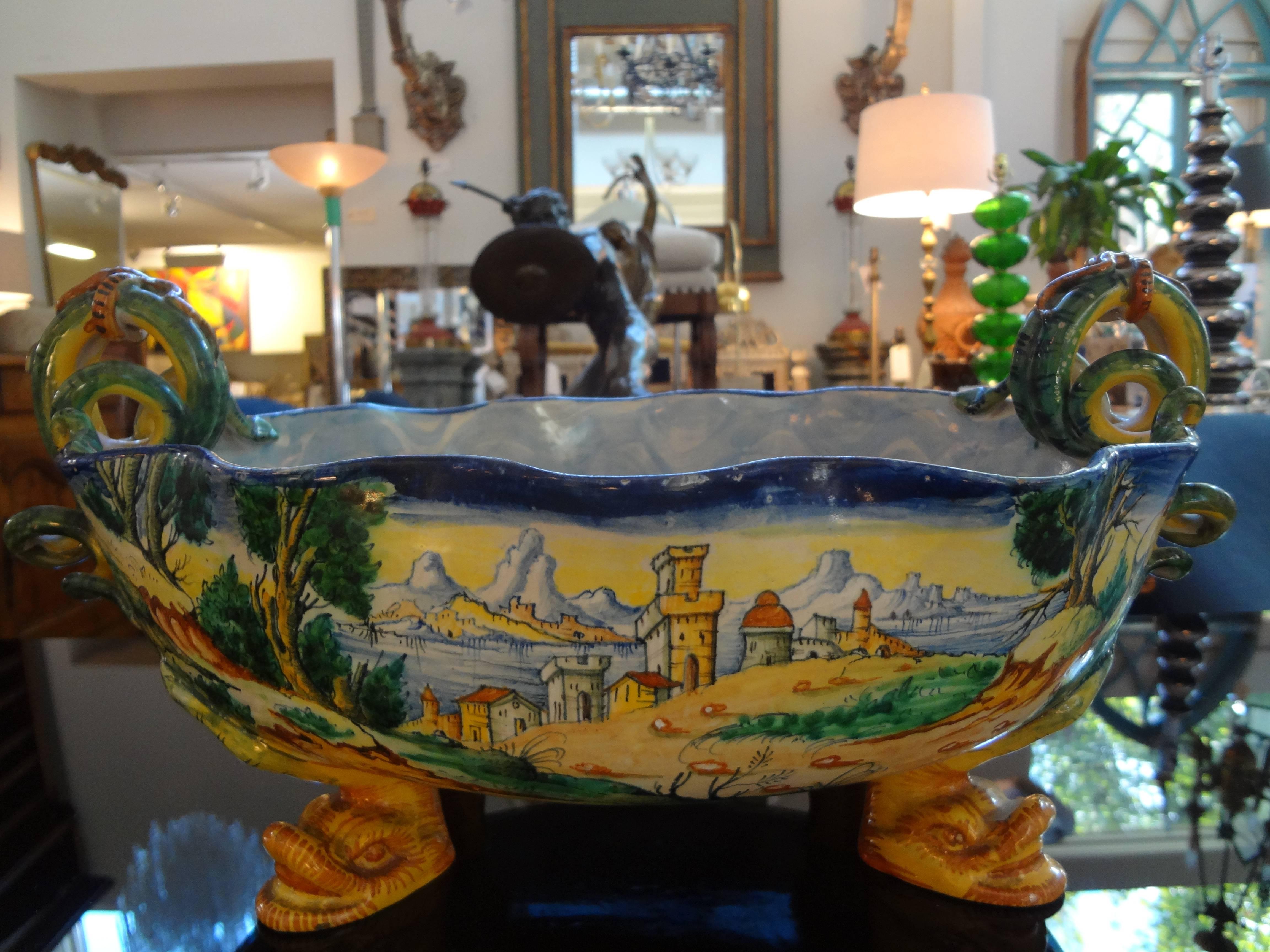 Beautifully hand decorated Classical Italian glazed pottery/majolica jardiniere, centerpiece or cachepot with serpent handles and dolphin feet with a village scene on one side and putti on the other.