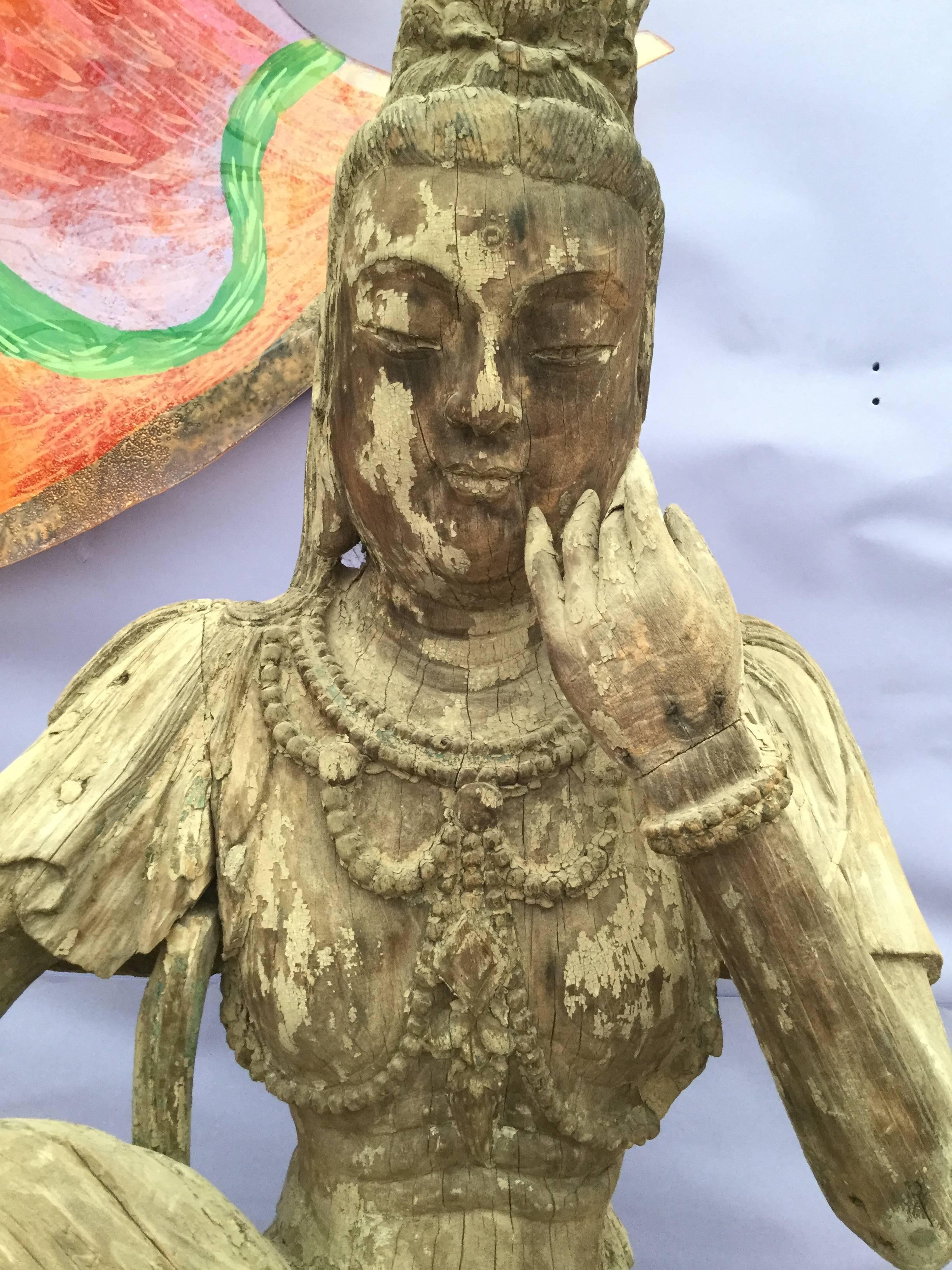 A beautiful Guan Yin carved wooden sculpture with a great worn and faded patina.
There are slight traces of color left but overall with faded patina. This Quan Yin is wearing an outstanding necklace and bracelets on each arm with hair twisted into