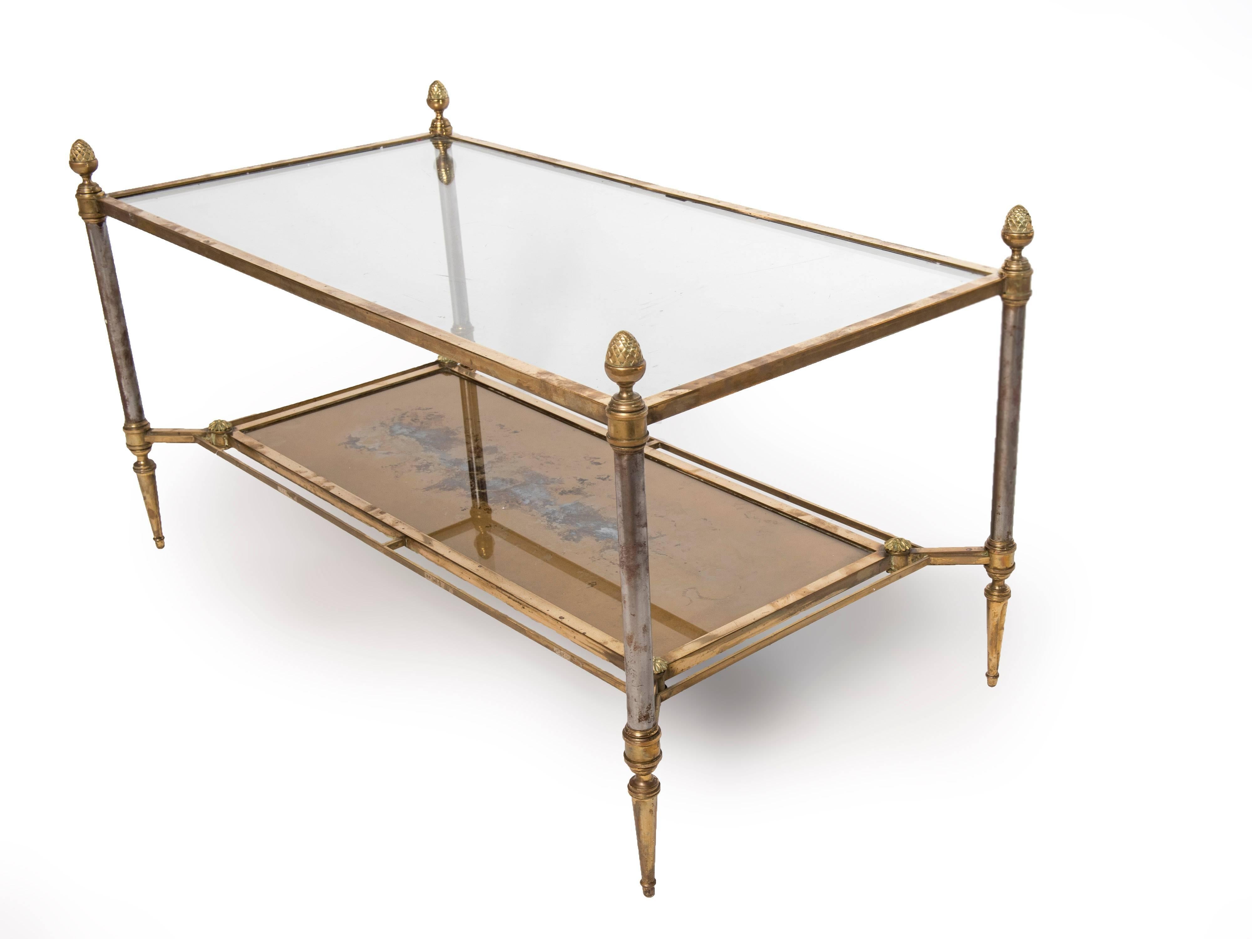 A rectangular brass-plated steel coffee table with a clear glass top and gold glass shelf below. The finials are solid brass. The posts are nickel plated which are showing some wear. The bottom gold glass shelf is worn from the underside which is