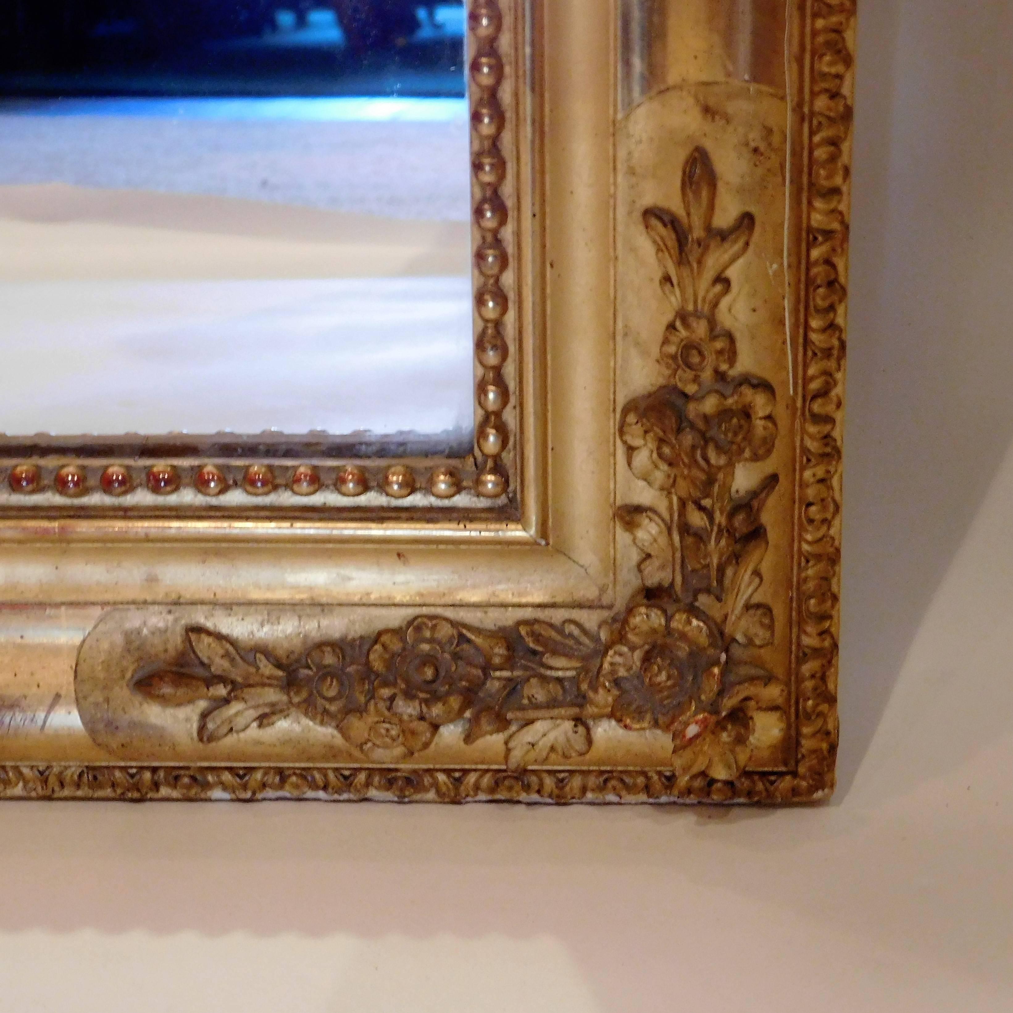 Gold leaf and gilt on gesso on wood, hand-carved ornament including over-mirror garland and putti, replaced glass, partial wooden back.