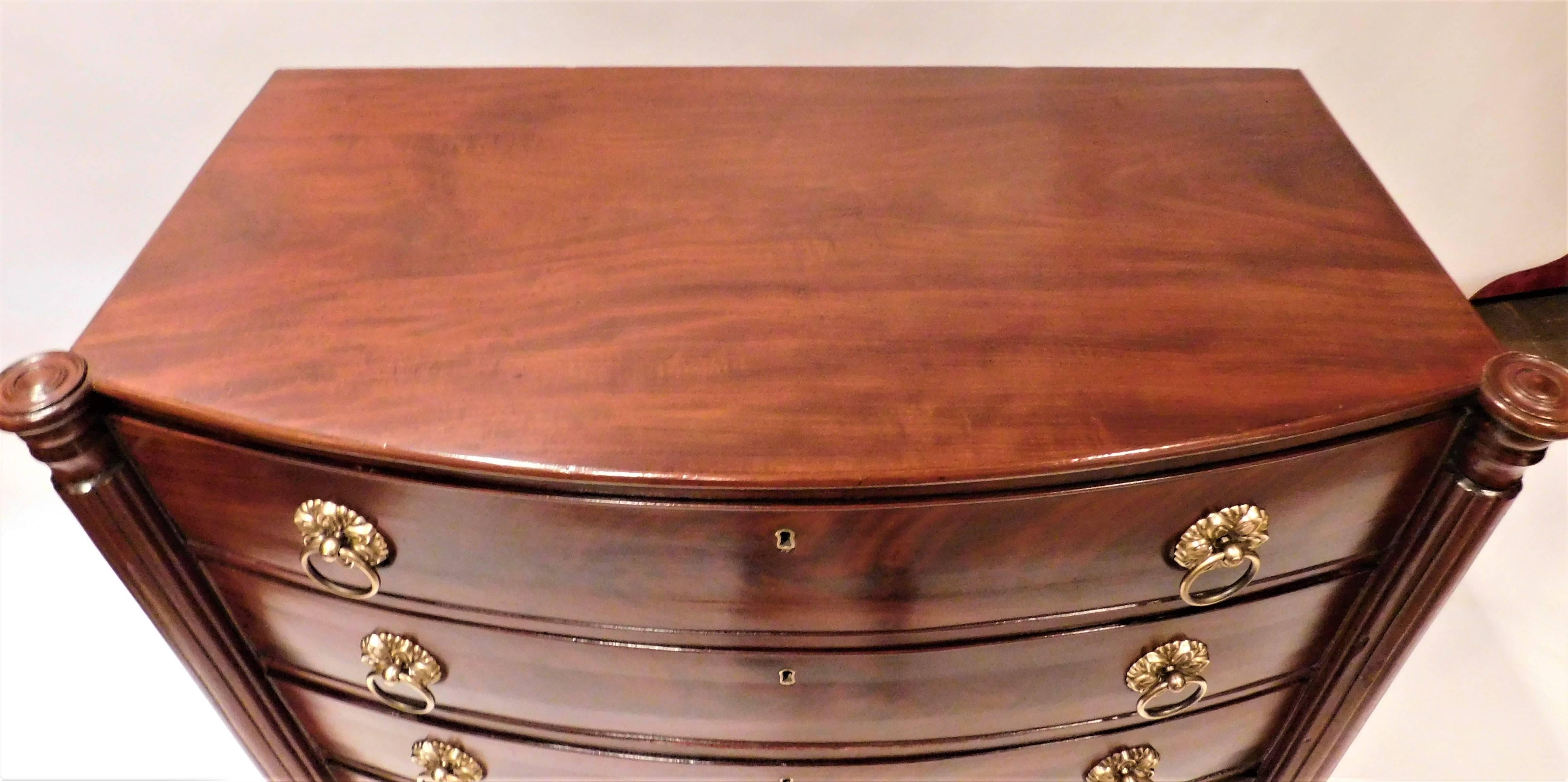 Flame mahogany fronts on the four drawers with mahogany top and case and pine secondary wood. New England, probably Massachusetts, French polish. Solid brass ring pulls. Turned legs. Single board top. Brass escutcheons. Drawers open and close