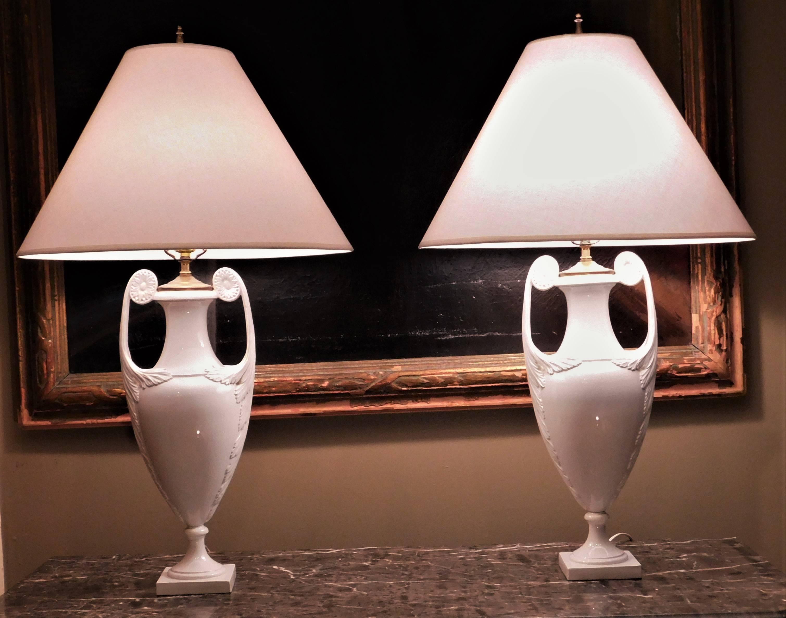 Each neoclassic urn now drilled and mounted as a lamp, with long neck above a baluster-form body with scrolled handles with paterae continuing to pendent foliage, on a square base. Dimensions shown exclude harp and shade, which are not included and