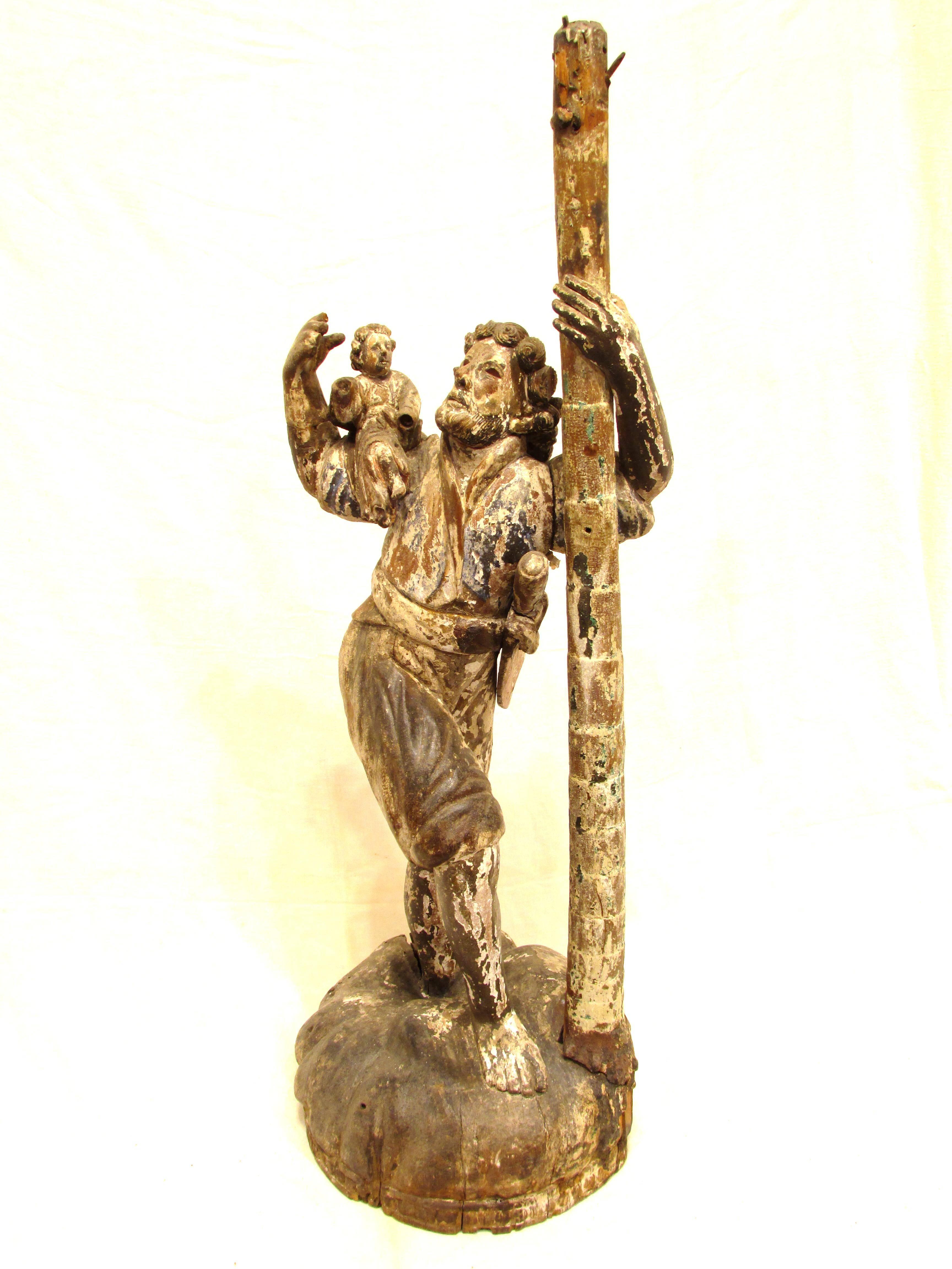 Antique and weathered carved wooden Santo of St. Christopher carrying the Christ child through water with tree for support in Conquistador attire.