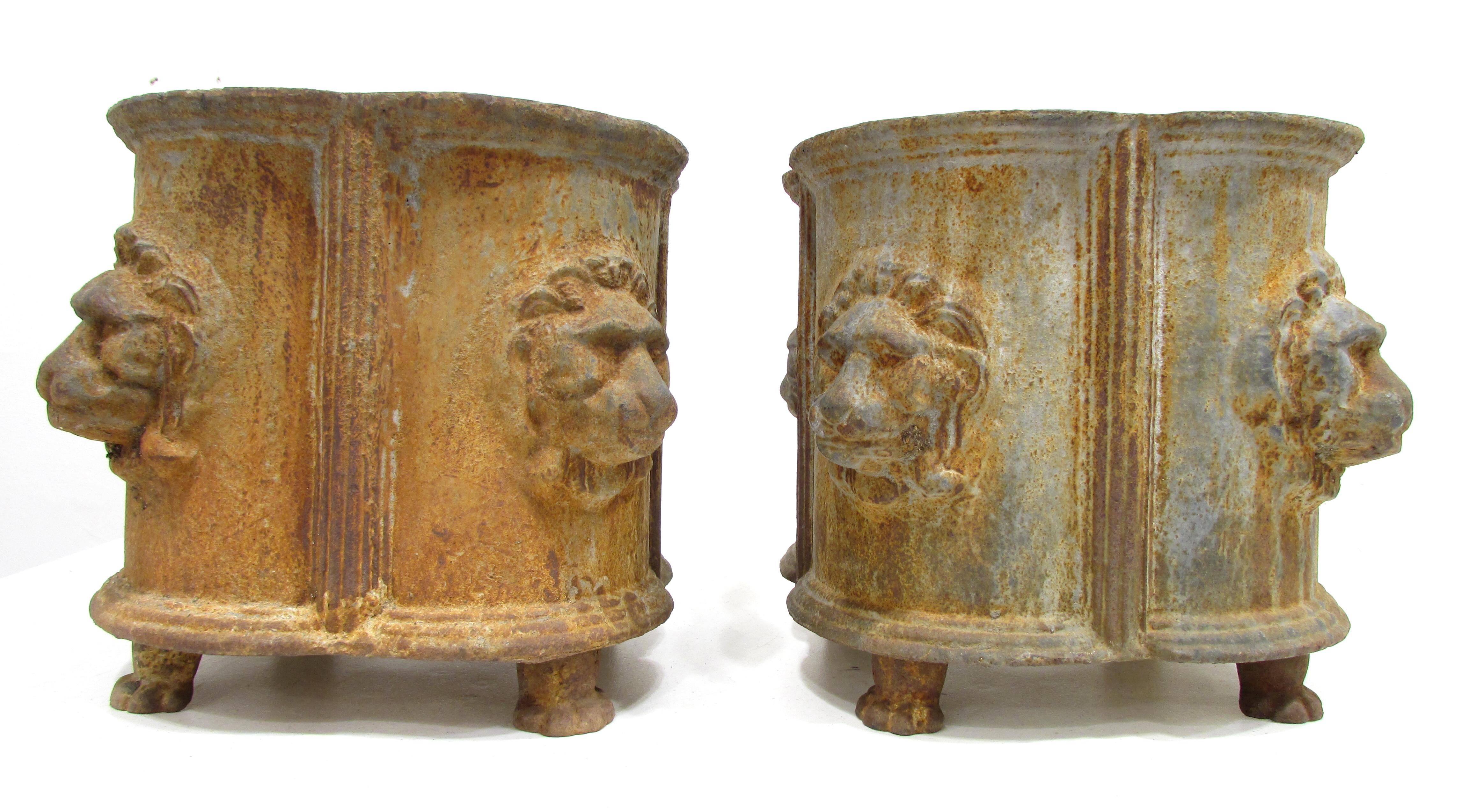 Pair of weathered heavy cast iron planters each with four lion's mask on sides and paw feet in Neoclassical style.