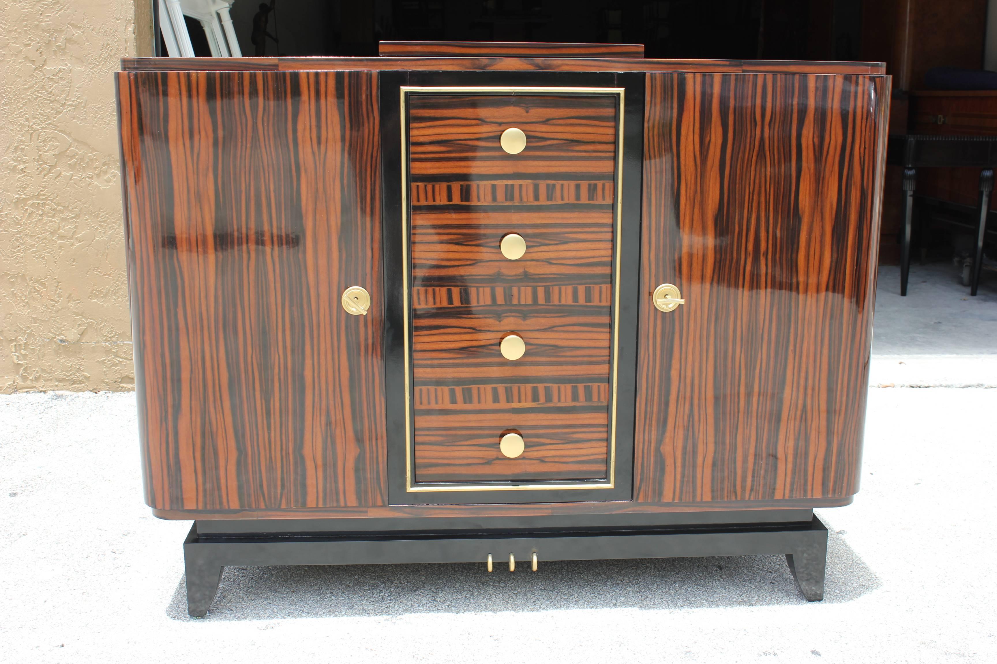 An absolutely stunning French Art Deco exotic macassar ebony bar/ buffet/ cabinet, circa 1940s. Black lacquer base. Top opens to reveal mirrored interior/ serving area. Center door opens to reveal totally mirrored interior with glass shelf. Center