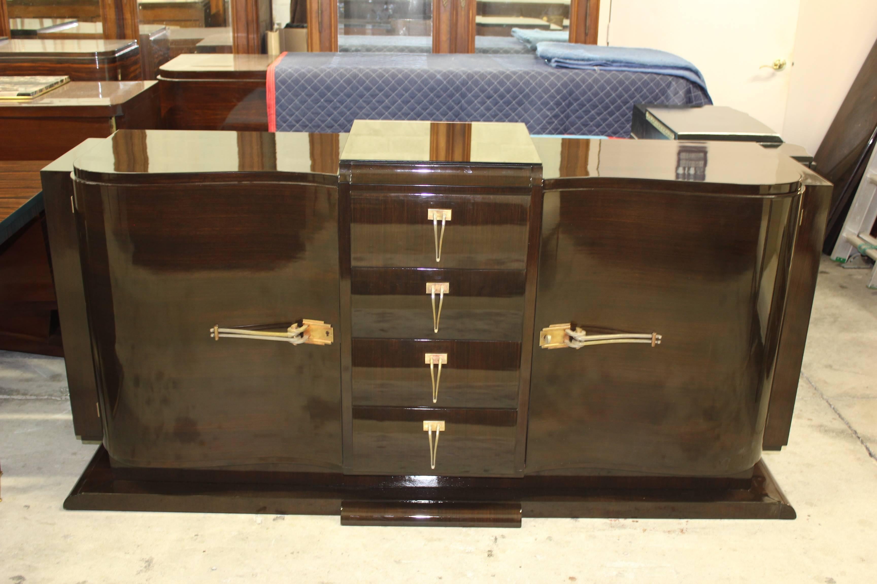 A stunning French Art Deco dark exotic Macassar Ebony Buffet/ Dry Bar, circa 1940s. Curved form, center bank of drawers. Elaborate hardware and gorgeous bronze tone mirrored center top panel for serving. There are glass shelves for the left and