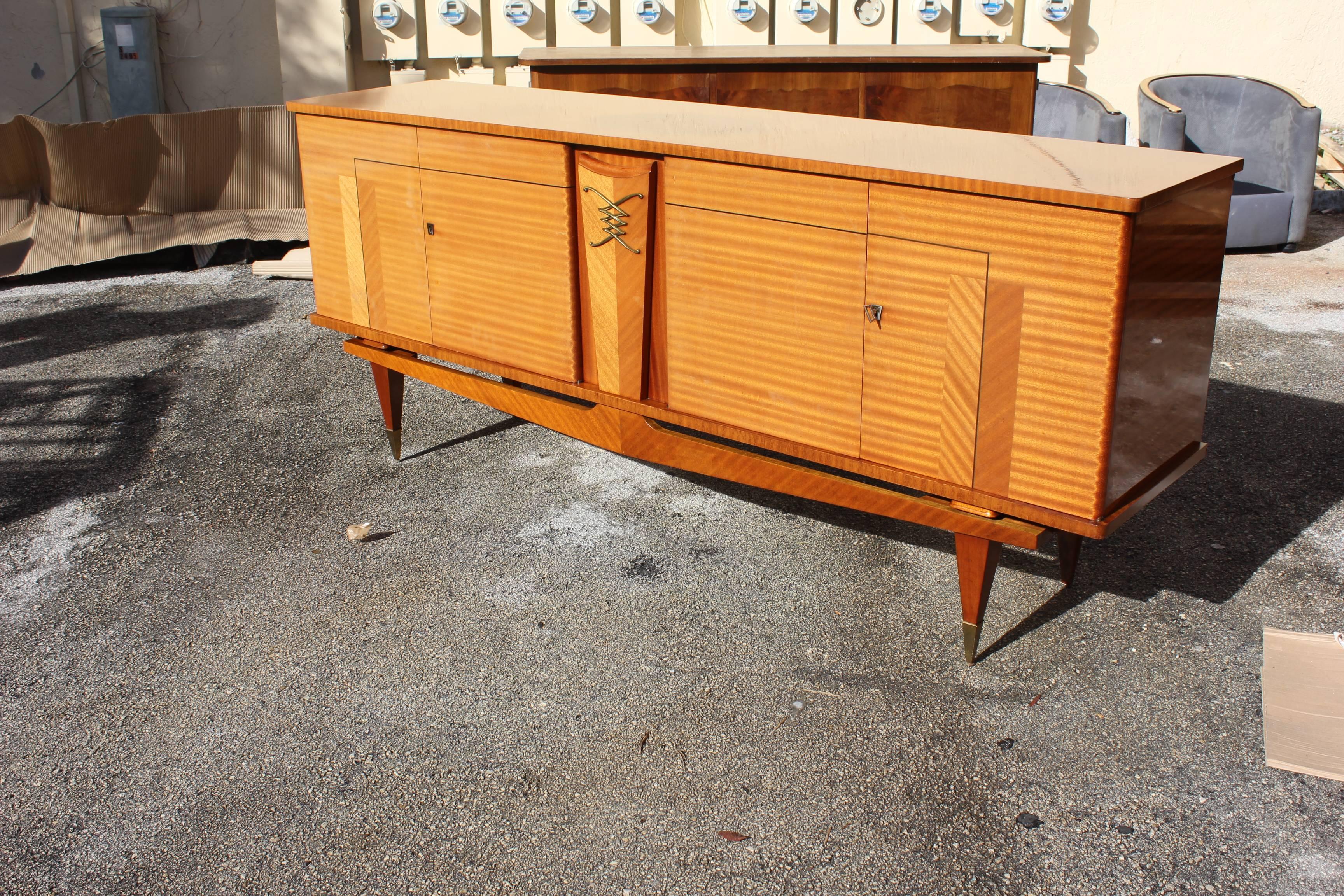 French Art Deco sideboard or buffet flame mahogany Ski Leg style, center bronze design, high gloss finish, circa 1940s. Please note these sideboard or buffets can be taken apart to accommodate elevator needs if necessary.