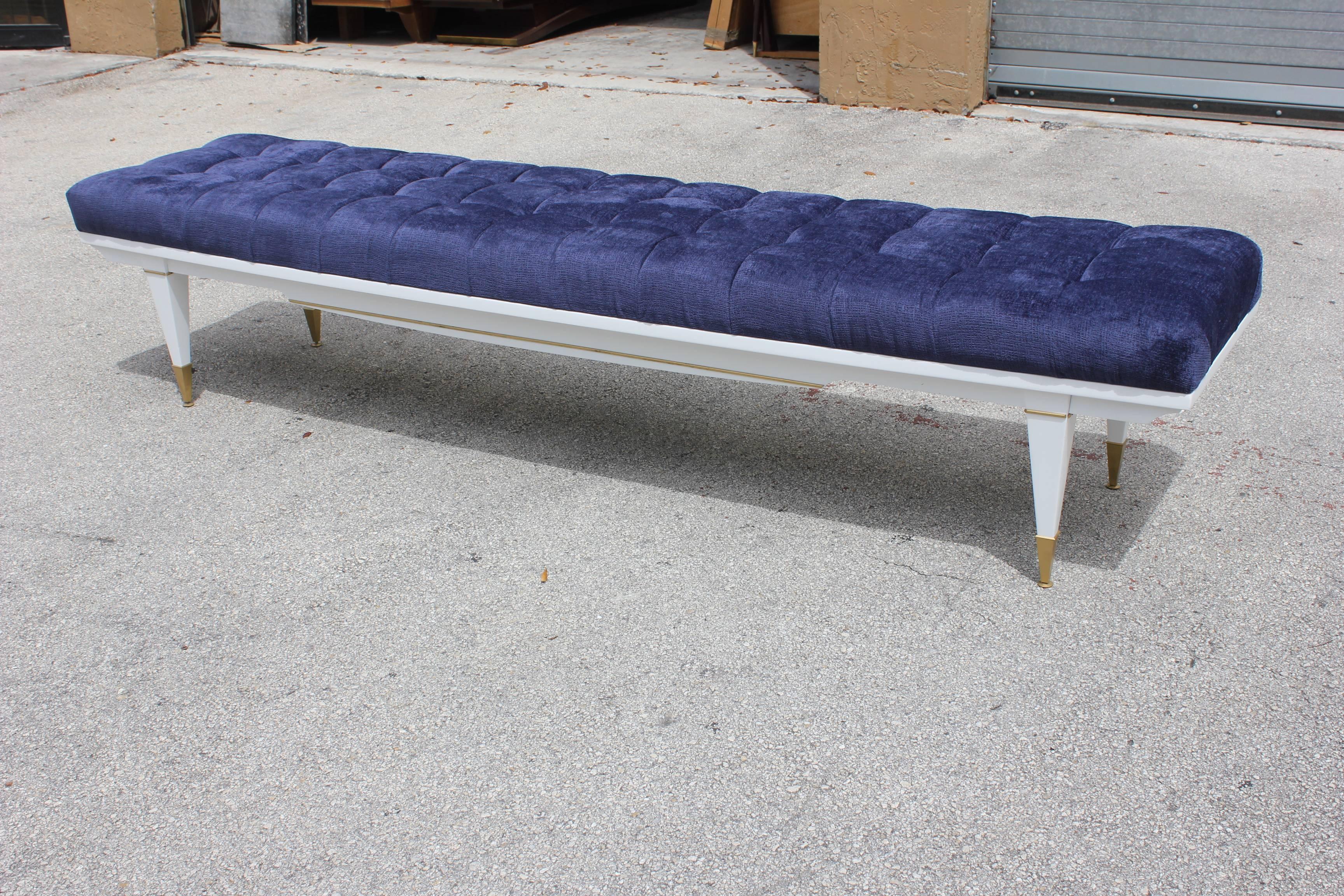 A long French Art Deco snow white lacquered sitting bench, circa 1940s. Newly upholstered in a very high textile velvet royal blue  . Newly refinished. White lacquer legs with brass caps.