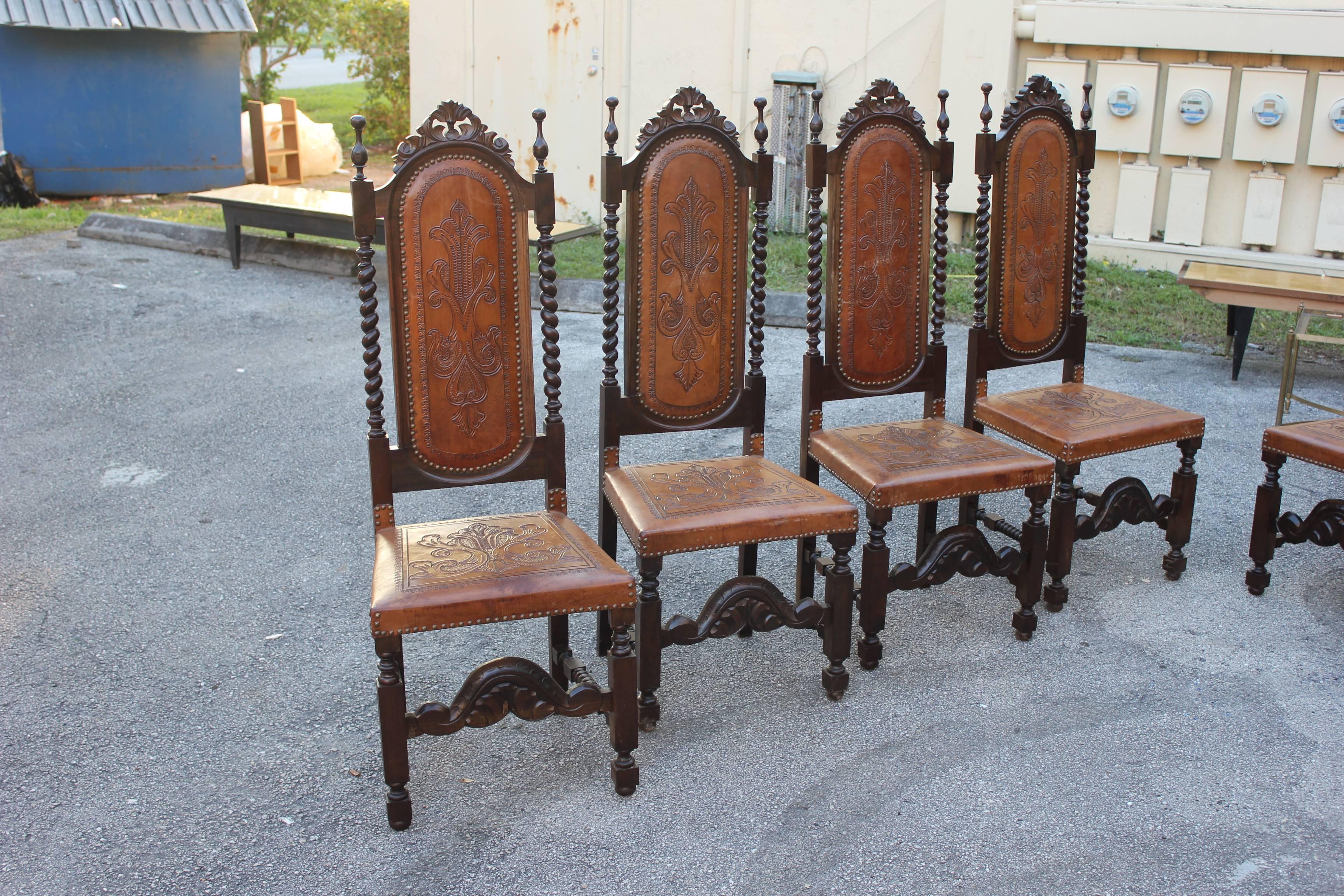 Monumental king of set eight Louis XIII style walnut and leather dining chairs from France. Original leather backs and seats, the intricate tooled leather design features typical neoclassical motifs. Supported by bobbin legs joined by turned