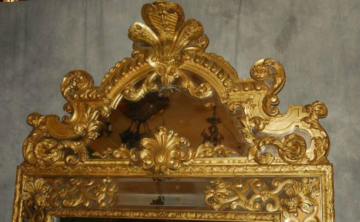 Large French Regence carved gilt-wood cushion mirror, the rectangular beveled glass mirror plate within a gilt-wood frame surmounted with a fleur-de-lis crest over an arched pediment with foliage and scroll carving. 