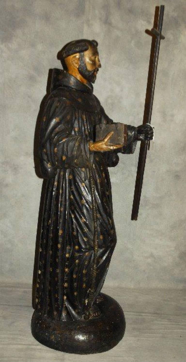 Large carved and polychrome wood figure of Saint Francis of Assisi with glass eyes and holding a book and cross. 

After 43 years of business we are retiring. Everything must be sold. Many of the pieces listed here on 1stdibs represent markdowns
