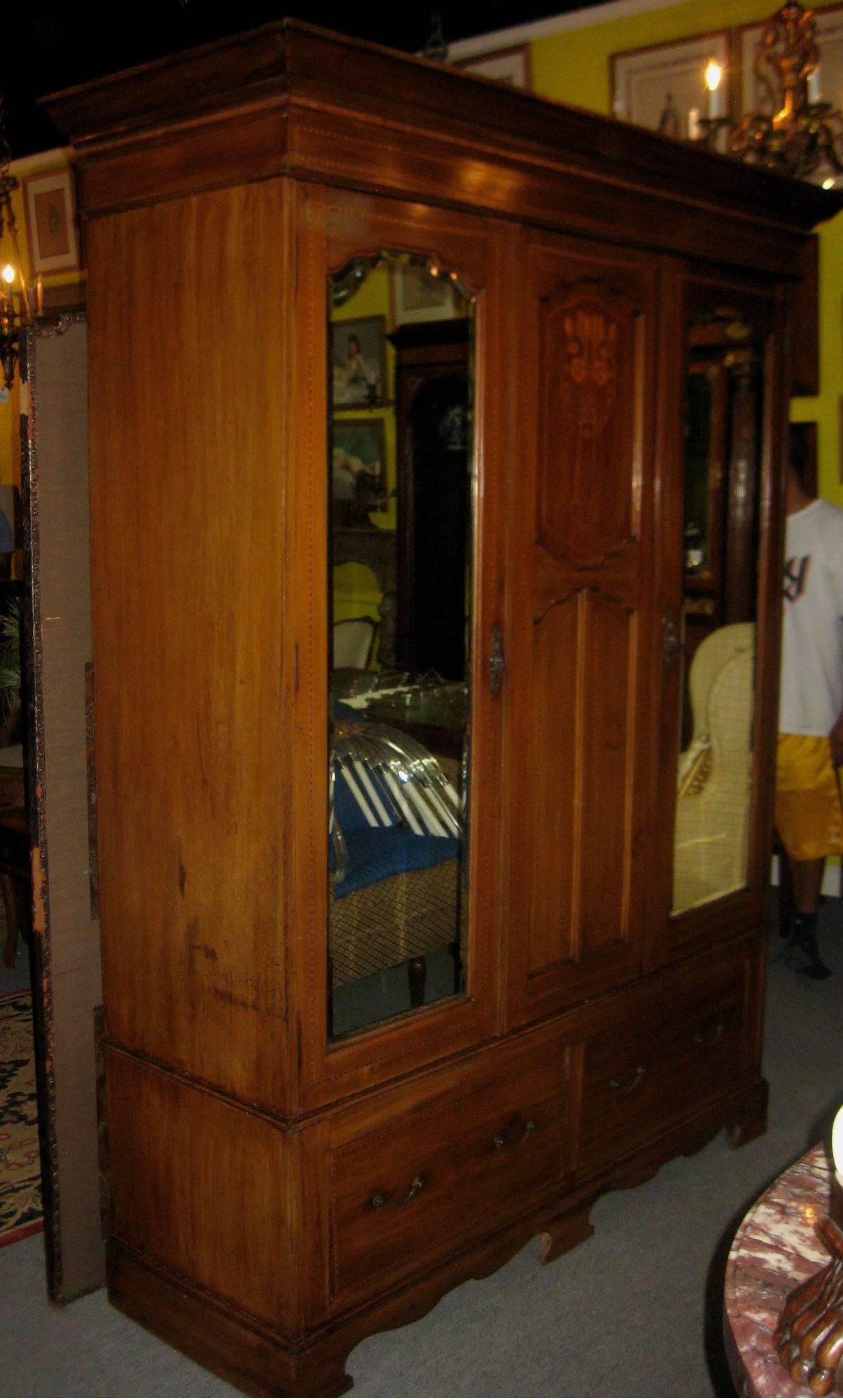 Art Nouveau inlaid mahogany two-door wardrobe or armoire with a molded overhanging cornice above a center inlaid panel flanked by mirrored doors; the left side opening to stationary brass hooks along the sides and back, a rotating three-sided hook