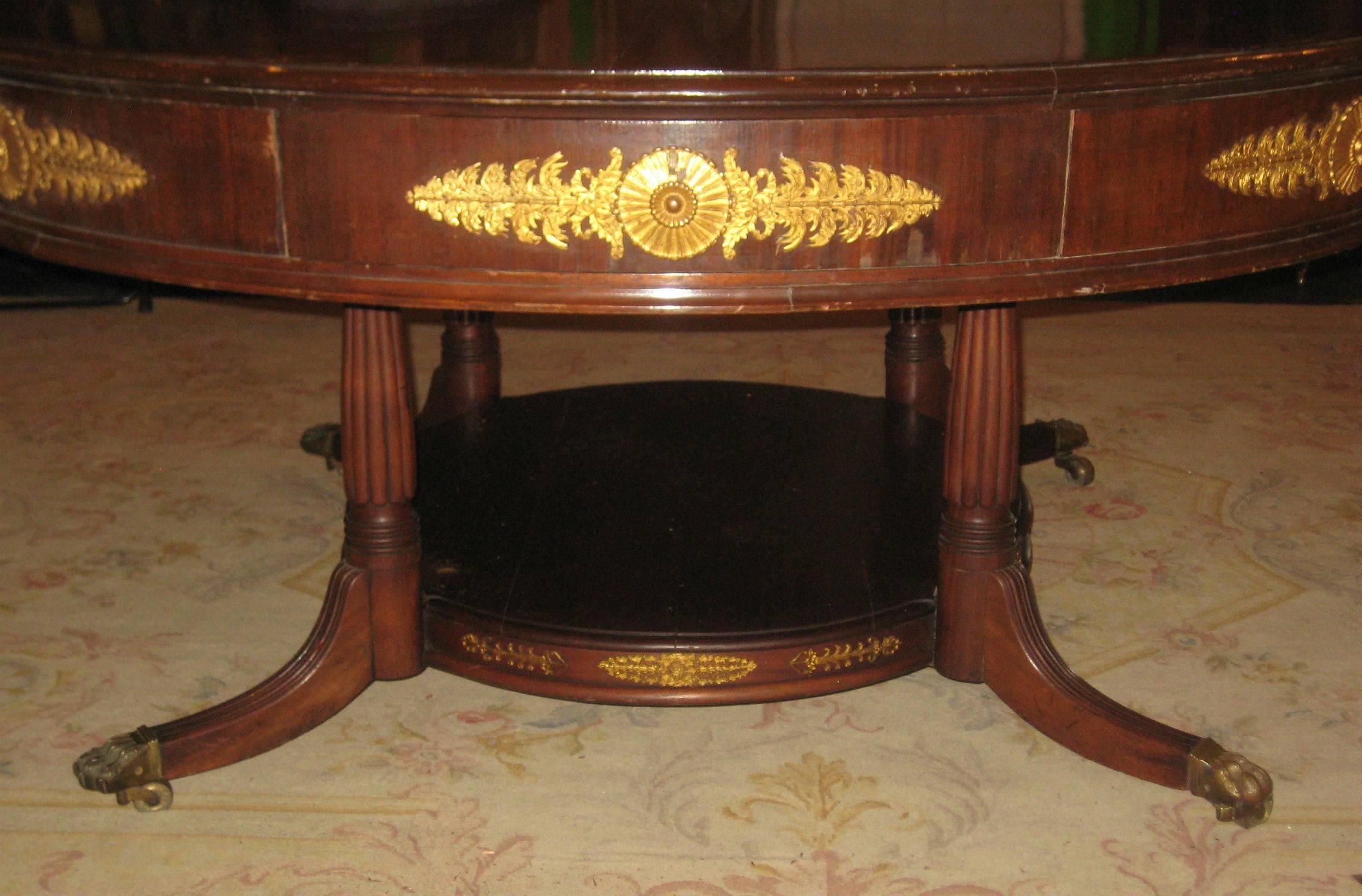 Large French Empire mahogany and gilt bronze-mounted four-drawer center table raised on fluted legs with a stretcher shelf base; the underside of the legs with the original iron leg braces, the down swept legs terminating with brass paws and casters.