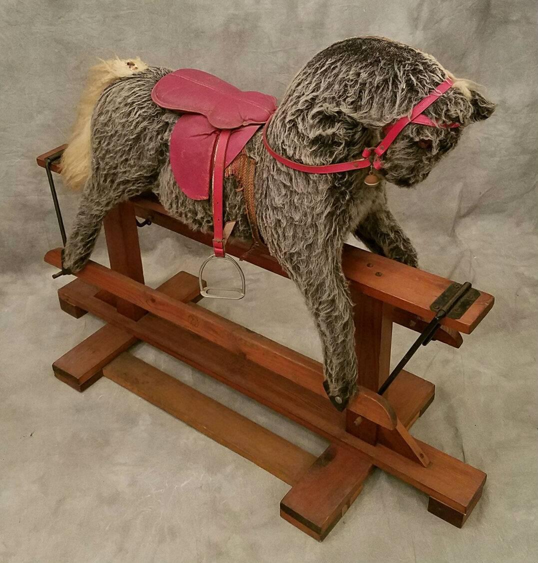 Vintage Pegasus gliding rocking horse with leather saddle and metal stirrups on a wood glide and base.