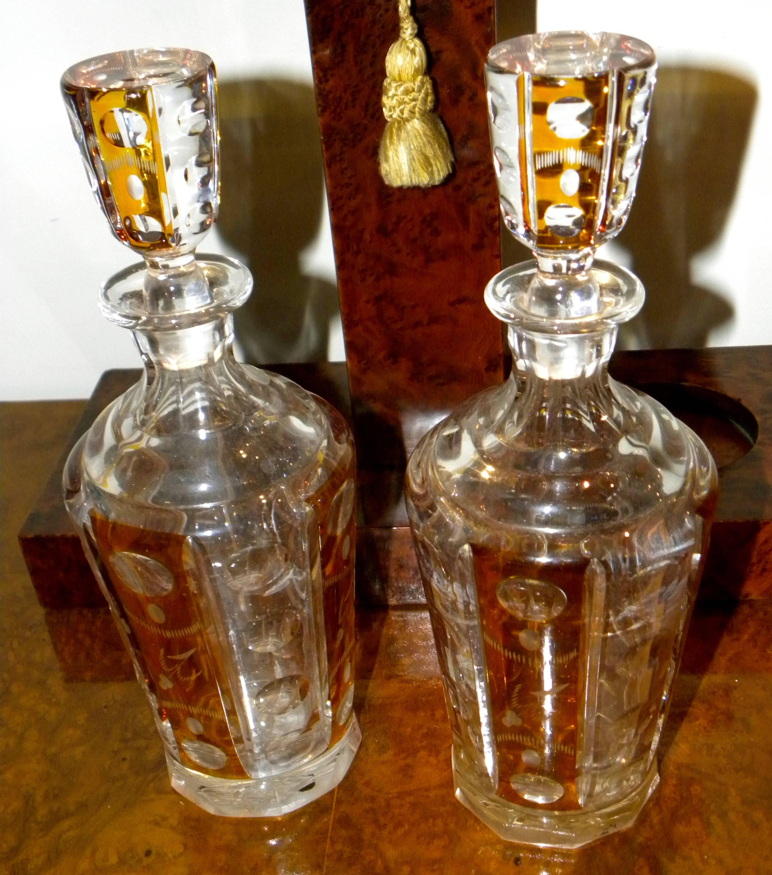 Elegant Art Deco tantalus stand and set. Two perfect cut-glass crystal decanters in an unusual amber color with matching top stoppers. This beautiful amboyna burl wood frames sets off the color of the glass in a unique way and holds the glass