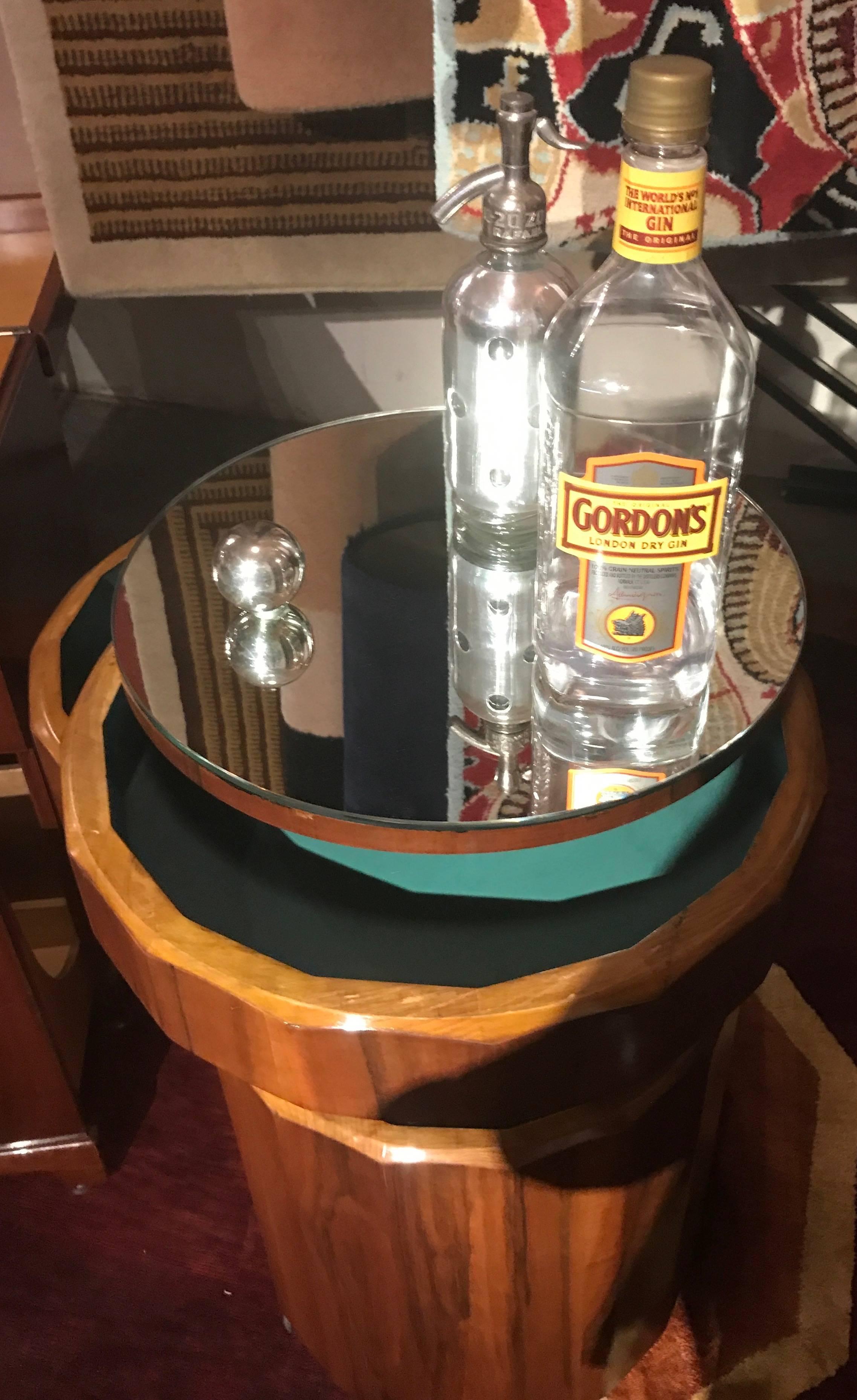 An Art Deco tyled bar cart, like an elegant ”Barrel of Fun” with fluted walnut exterior and green felt lined interior and all of it mounted on casters and “ready to roll”. When closed, with its smartly mirrored top it makes a slim side table, then