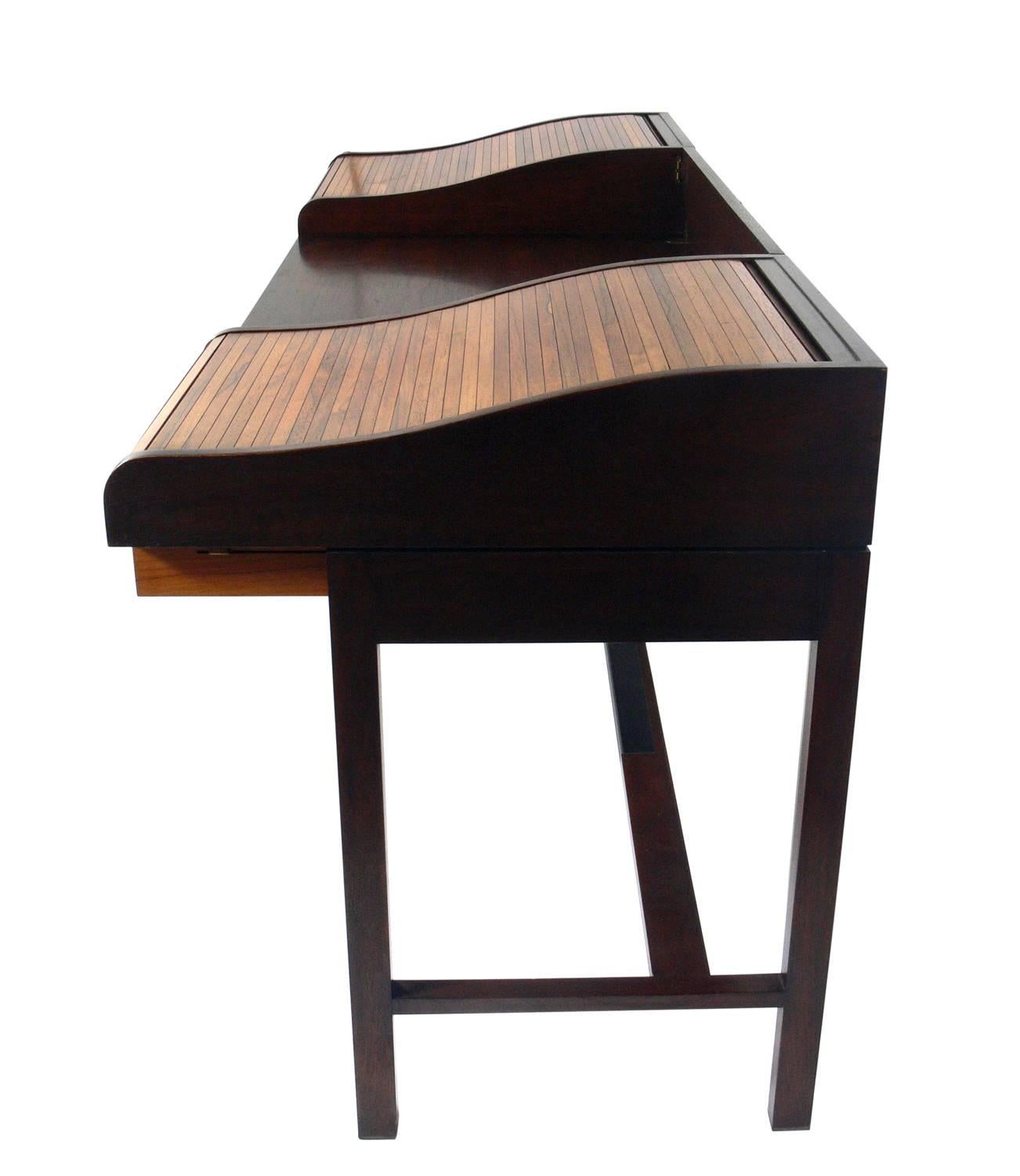 Rosewood and mahogany roll top desk, designed by Edward Wormley for Dunbar, American, circa 1960s. The tambour roll up doors open to reveal additional work space and storage areas and the back rail folds down to make this a partners desk. Signed