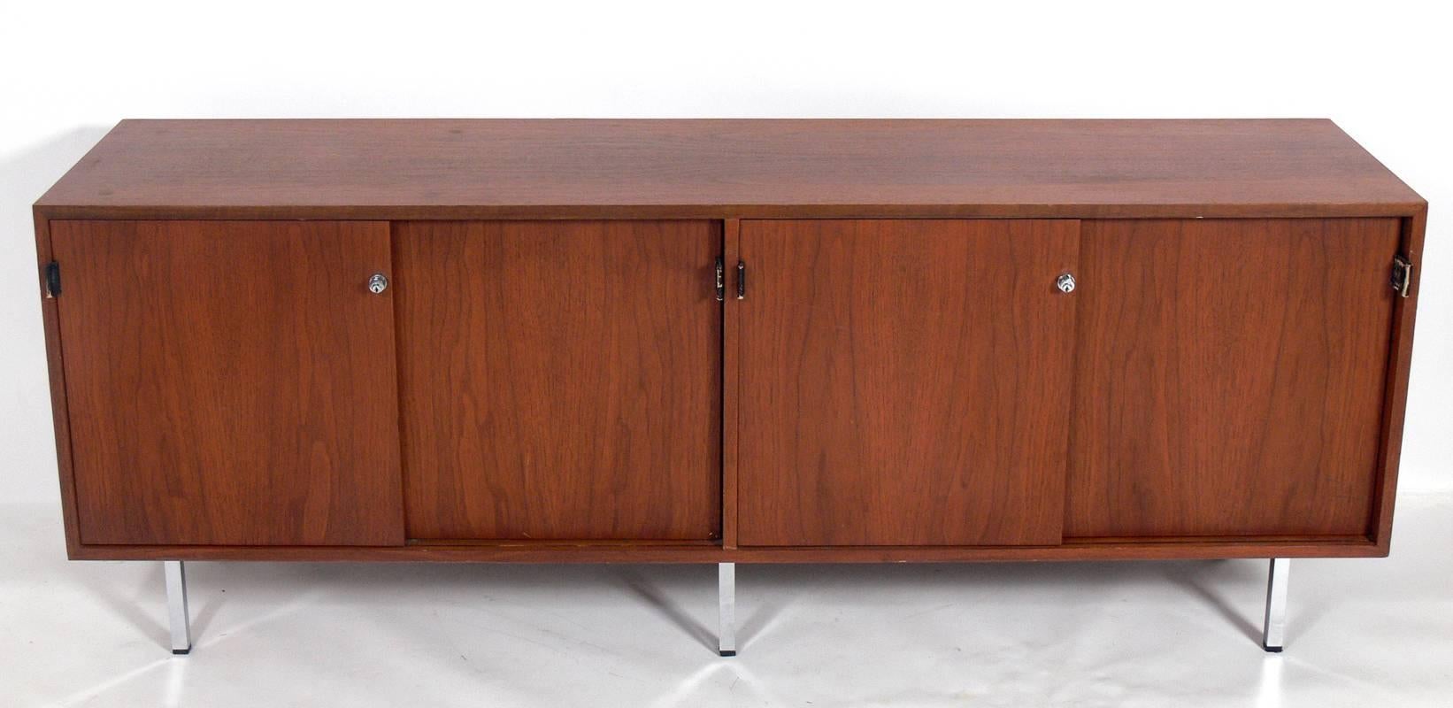 Clean Lined Walnut Credenza, designed by Florence Knoll for Knoll Associates, circa 1970's. This piece offers a voluminous amount of storage with four sliding doors that open to reveal three wide drawers, three shelves, and four drawers. If you