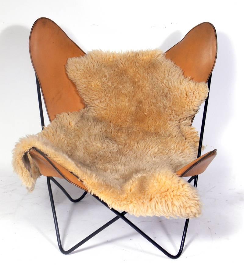 Sculptural leather sling chair by Jorge Ferrari Hardoy, circa 1950s. This chair retains it's original caramel color leather sling seat. The leather sling seat has a lot of scratches, patina and wear, but looks great with the sheepskin draped over