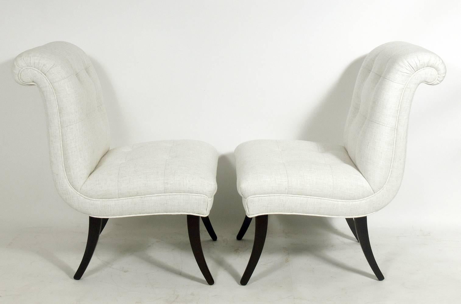 Paire de fauteuils pantoufles aux formes arrondies, américains, vers les années 1940. Une forme glamour avec des dossiers à volutes spectaculaires, des boutons touffetés et des pieds aux courbes sexy. Rembourré dans une tapisserie de style lin