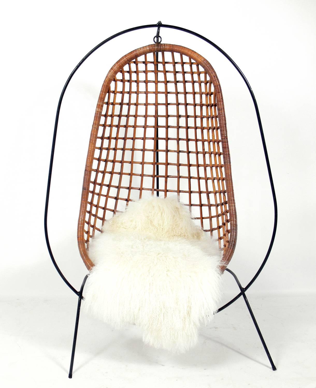 Sculptural iron and rattan hanging chair with Mongolian lamb throw, American, circa 1960s. The iron and rattan combine to give this piece a real California Modern vibe. Newly upholstered cushion and Mongolian lamb throw.