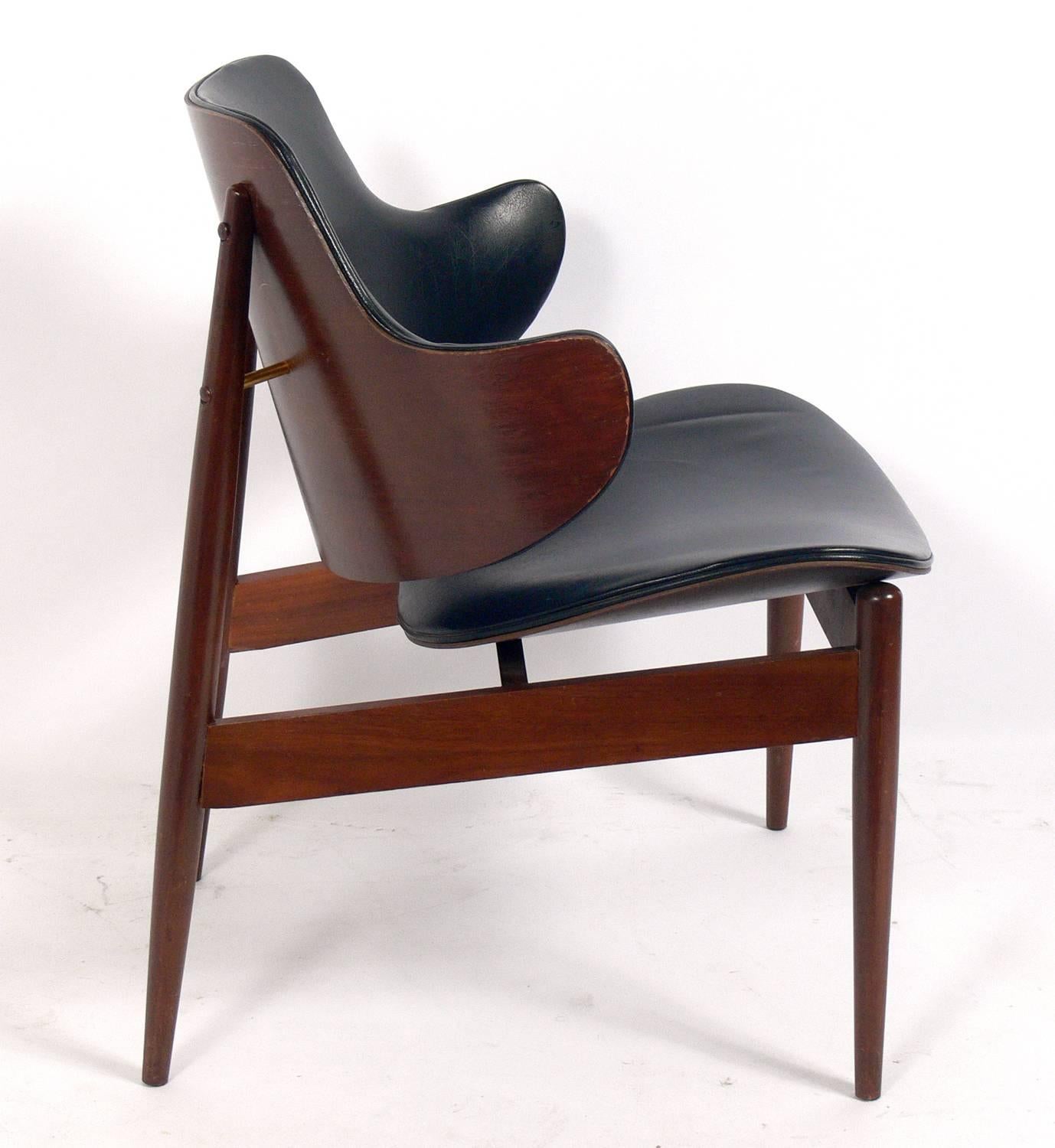 Curvaceous Danish Modern lounge chair attributed to Ib Kofod-Larsen, Danish, circa 1960s. It retains its warm original patina and original black vinyl upholstery.